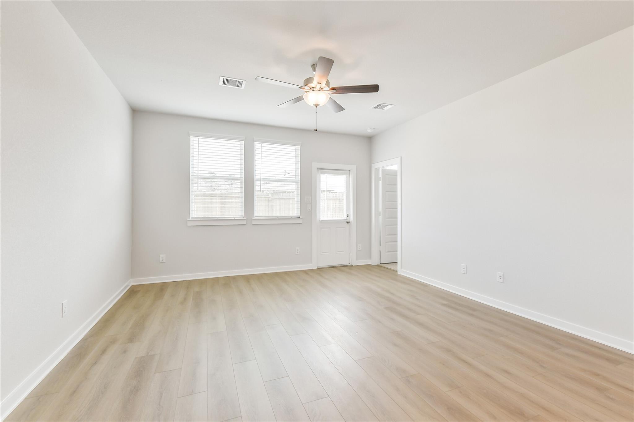 Bright living room with ceiling fan, large windows, French door, and light hardwood floors in Davidson Homes Colorado F, Cleveland TX