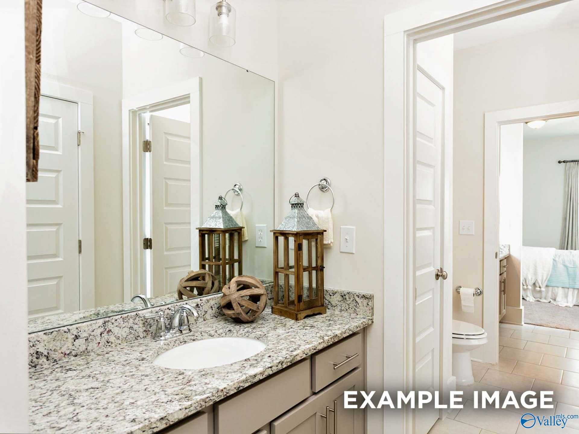Elegant master bathroom with granite vanity, double mirrors, wooden lanterns, and adjacent bedroom in Davidson Homes The Finleigh, Meridianville, Alabama