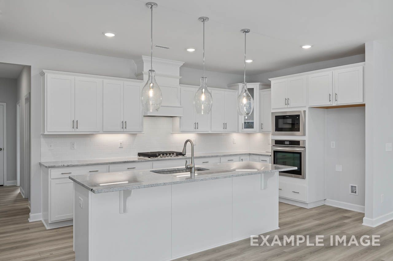Modern kitchen with white cabinetry, granite countertops, and stainless steel appliances at Retreat at North Main in Lillington