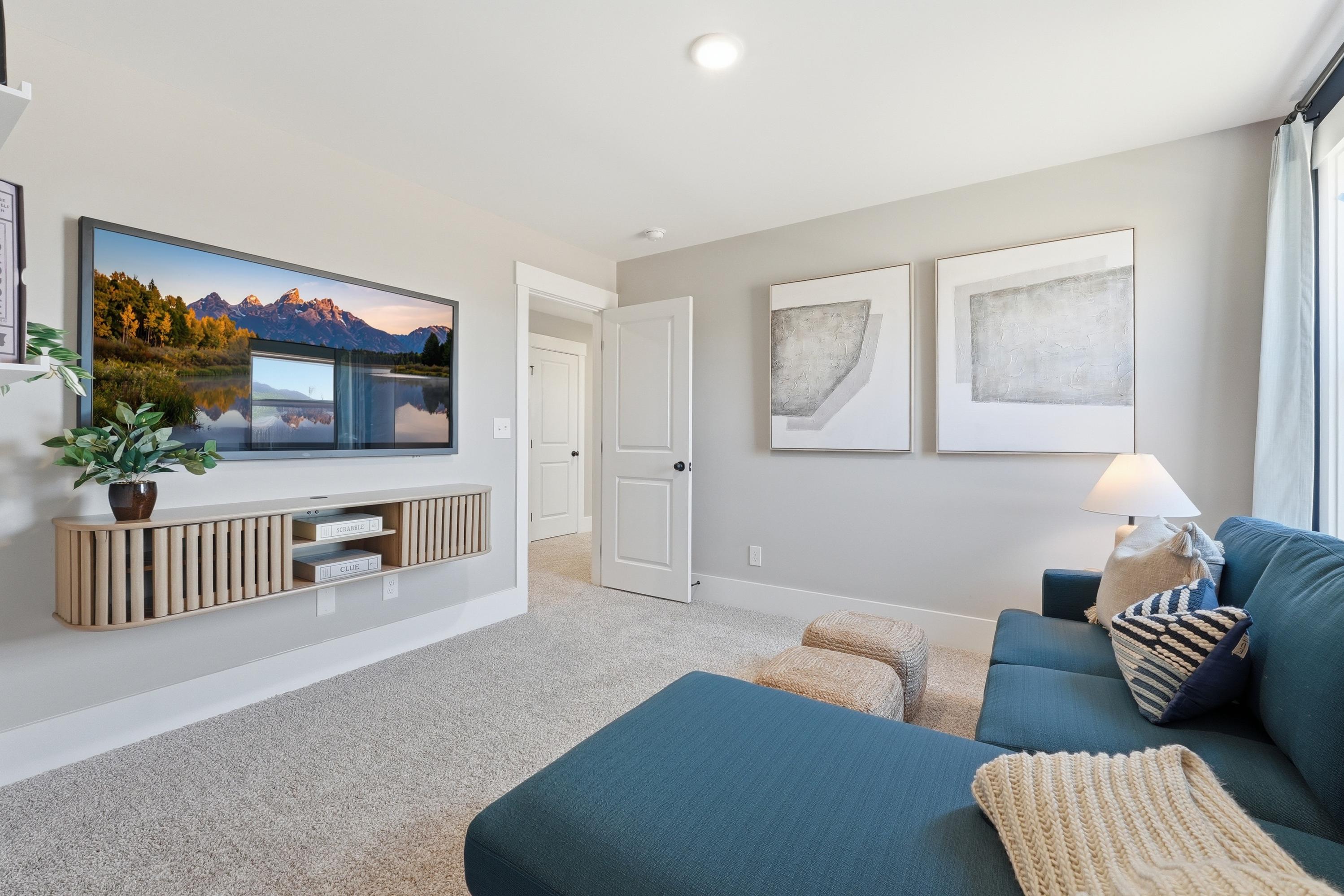 Cozy media room in Berry Cove home with wall-mounted TV, teal L-shaped sofa, floating wood shelf, and modern art in New Market, Alabama