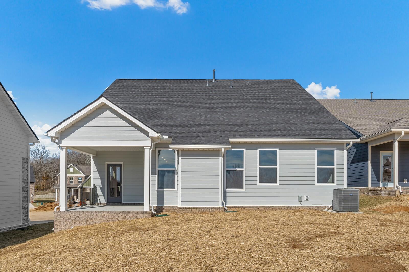 Rear view of The Ash A two-story gray home with covered patio, large windows, and expansive backyard in Woods Crossing, Gallatin, Tennessee