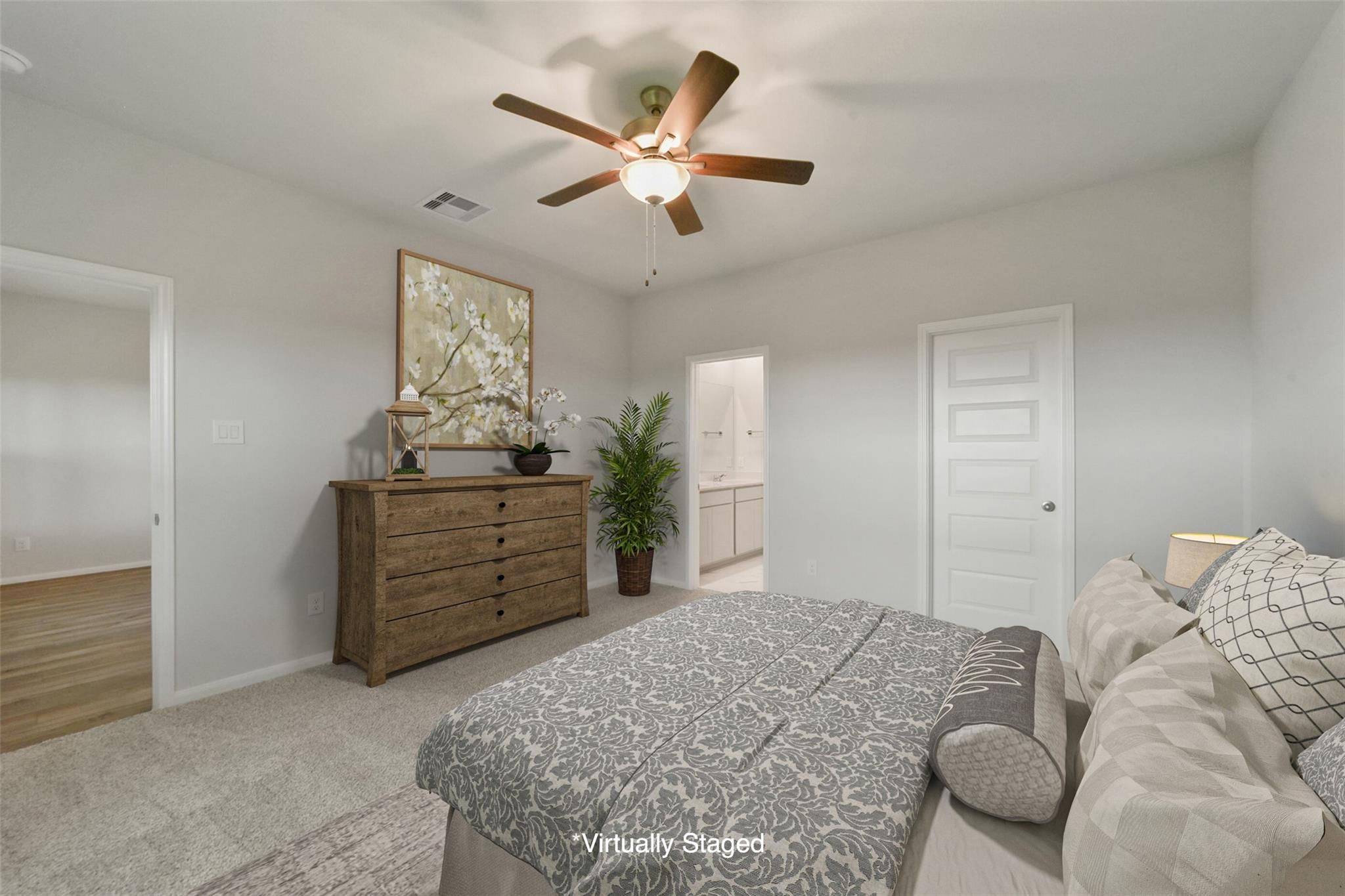 Cozy bedroom with ceiling fan, wooden dresser, potted plant, floral art, plush gray bed, en-suite bath in Davidson Homes San Marcos E, Beasley TX