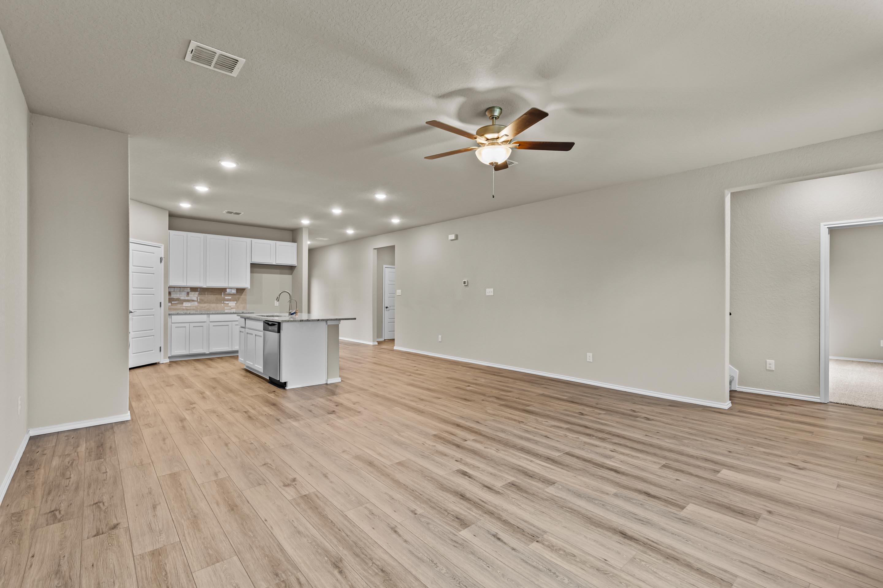 Spacious open kitchen with white cabinets, center island, ceiling fans, and hardwood floors in Davidson Homes Douglas F, San Antonio