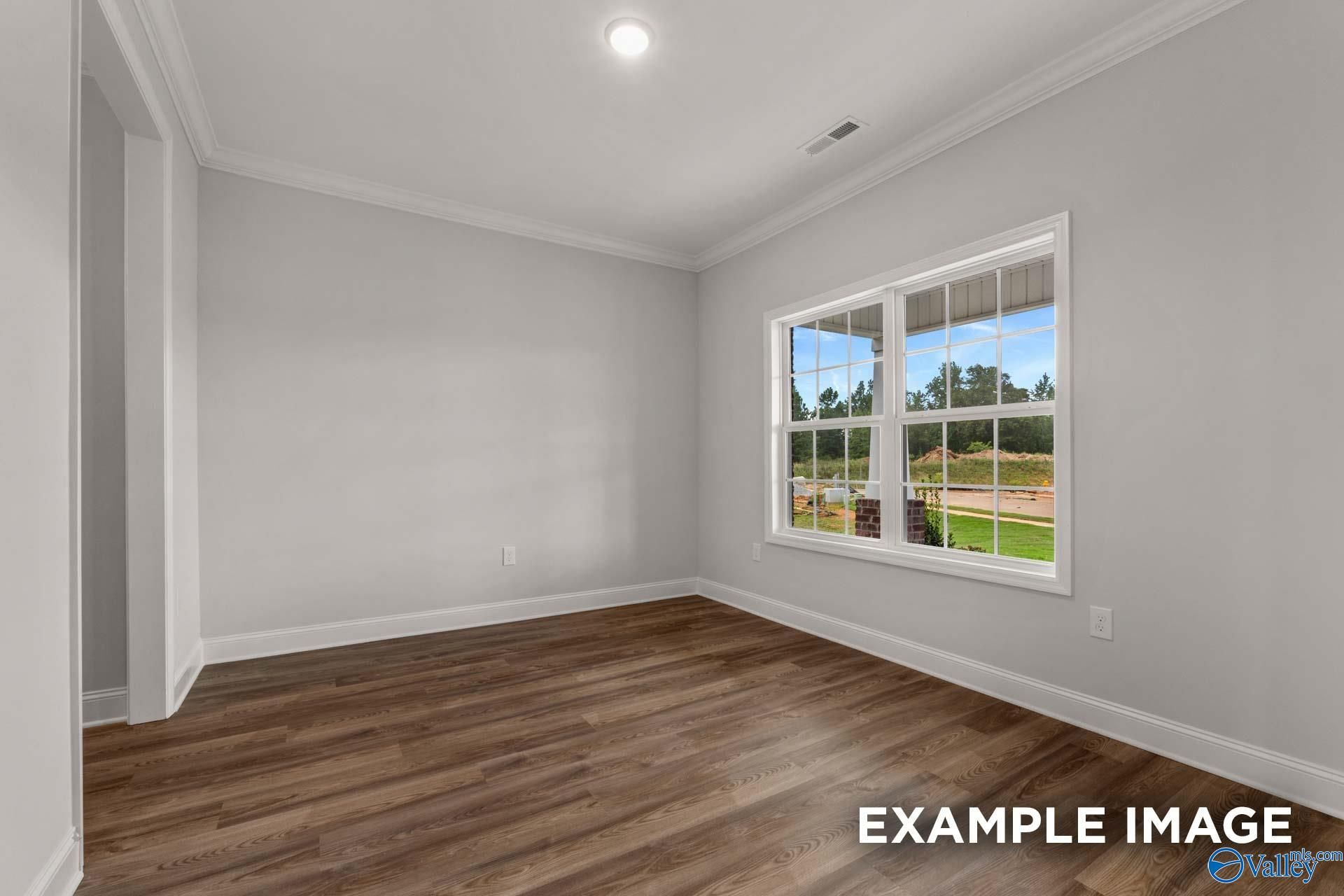 Spacious empty bedroom with light gray walls, hardwood floors, and large window overlooking wooded yard in The Shelby C home, Arab, Alabama