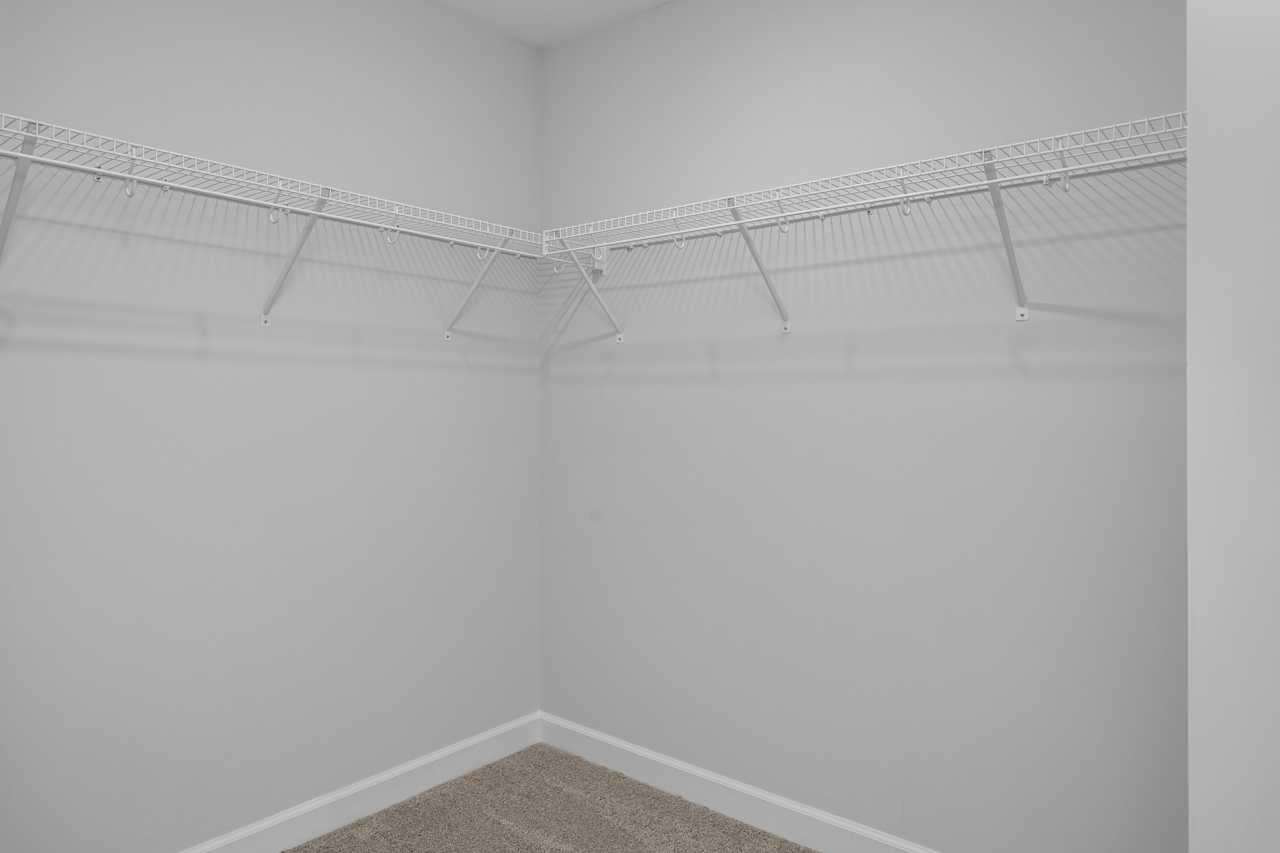 Spacious walk-in closet in The Durham master suite featuring wire shelving, gray walls, and beige carpet by Davidson Homes