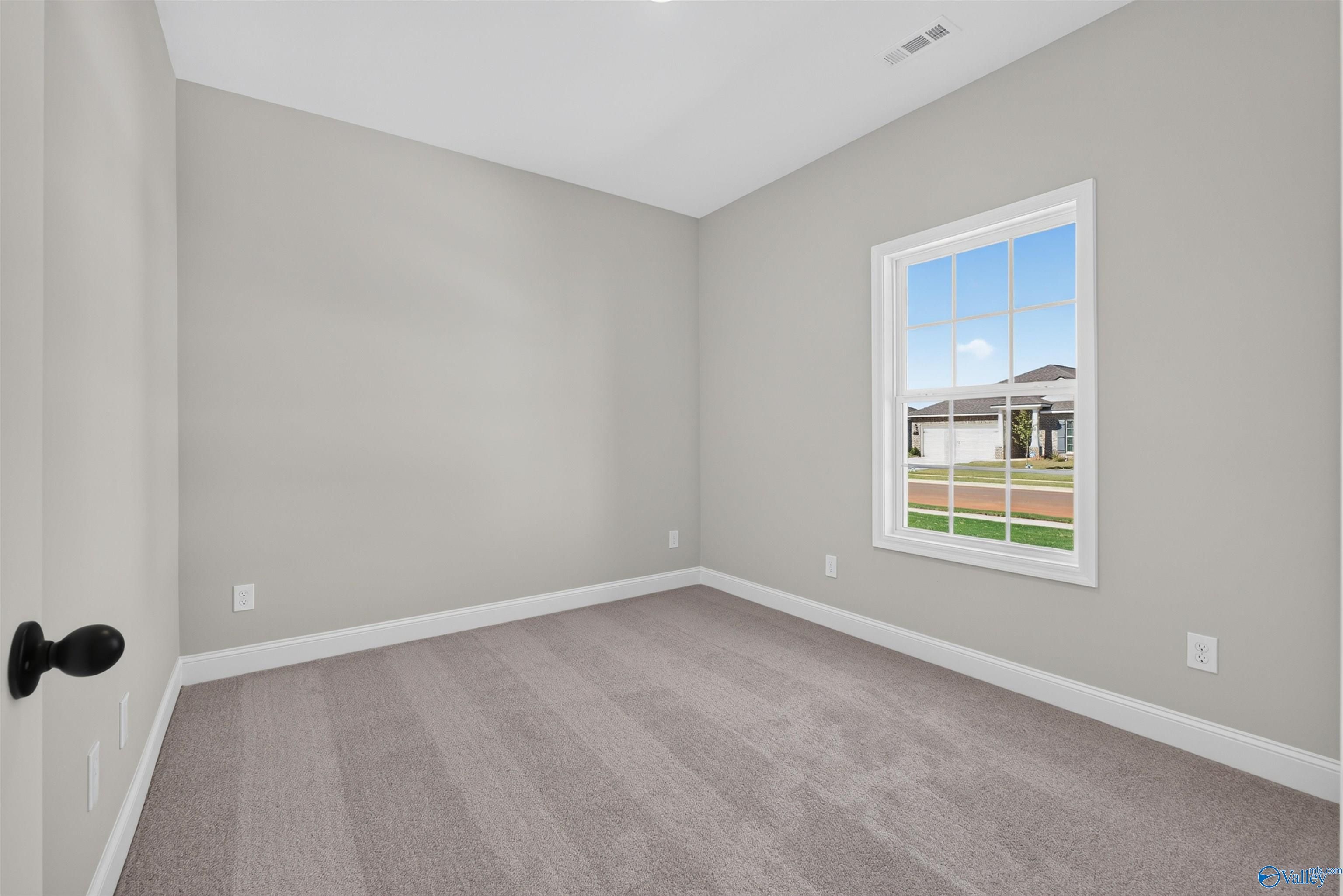 Bright empty bedroom with neutral walls, carpet, and white-trimmed window in Davidson Homes The Butler floor plan, Hazel Green, Alabama