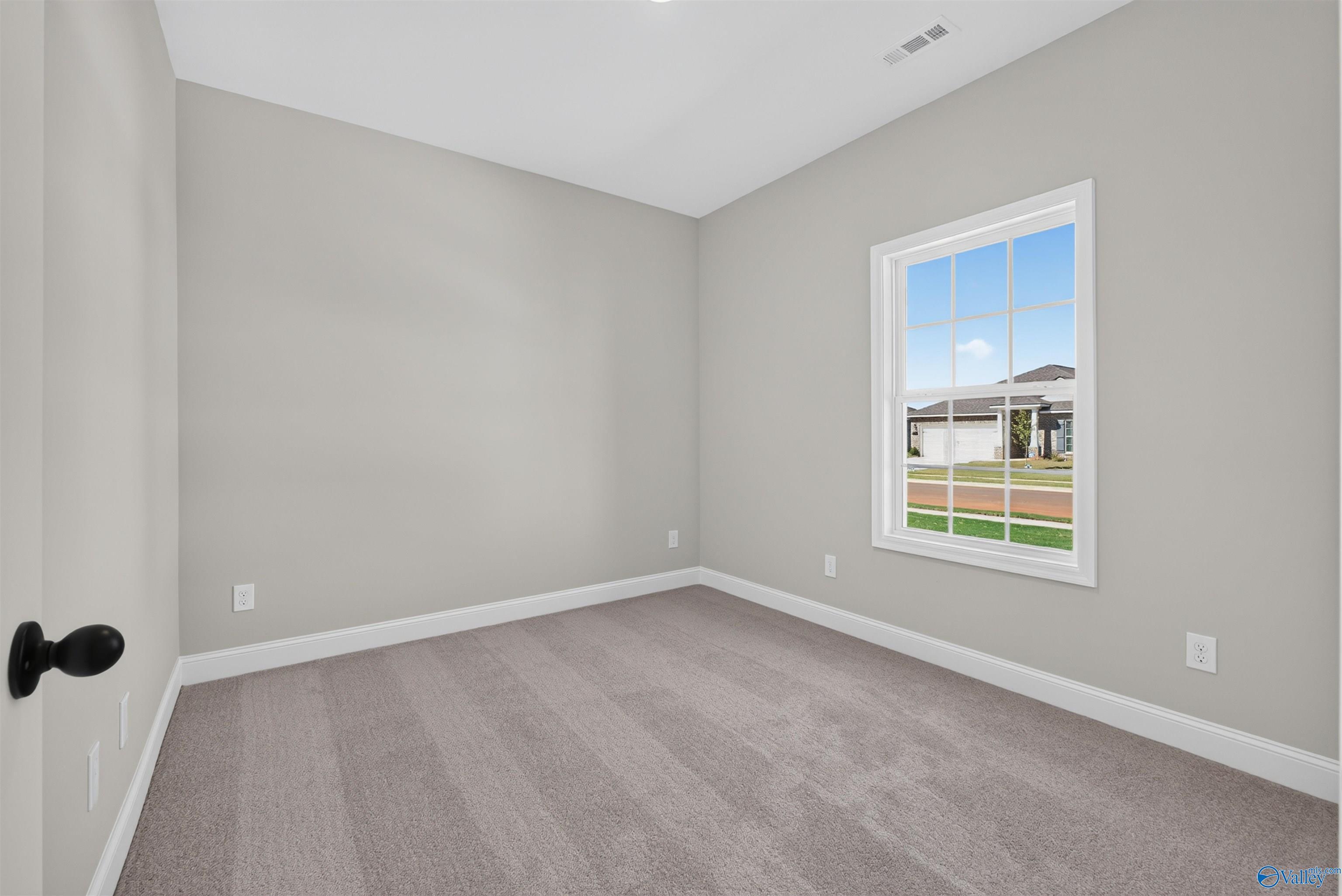 Bright empty bedroom with neutral walls, carpet, and white-trimmed window in Davidson Homes The Butler floor plan, Hazel Green, Alabama