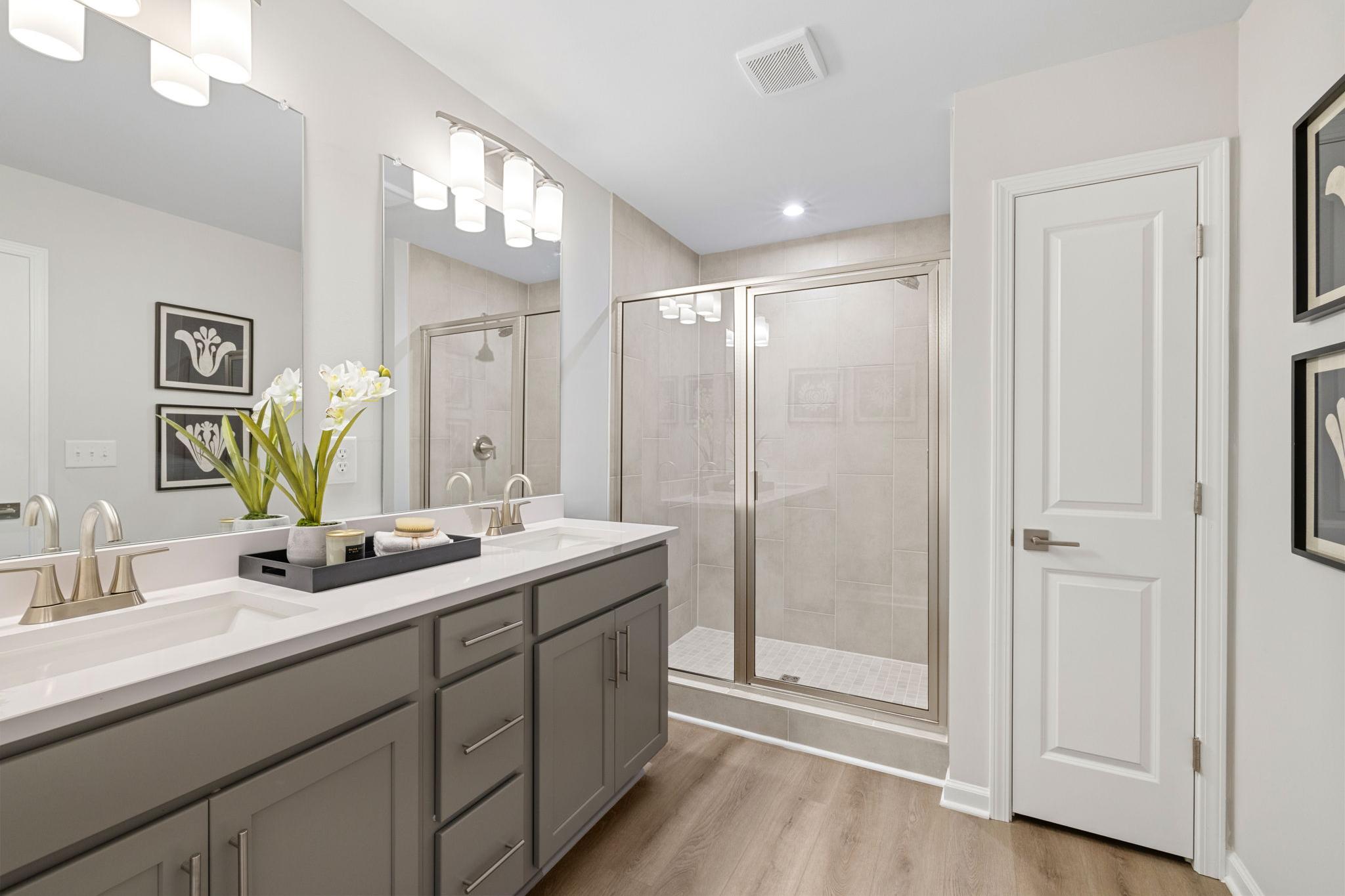 Modern primary bathroom at Lake Shore in Winder, Georgia with double vanity, glass shower, and hardwood floors