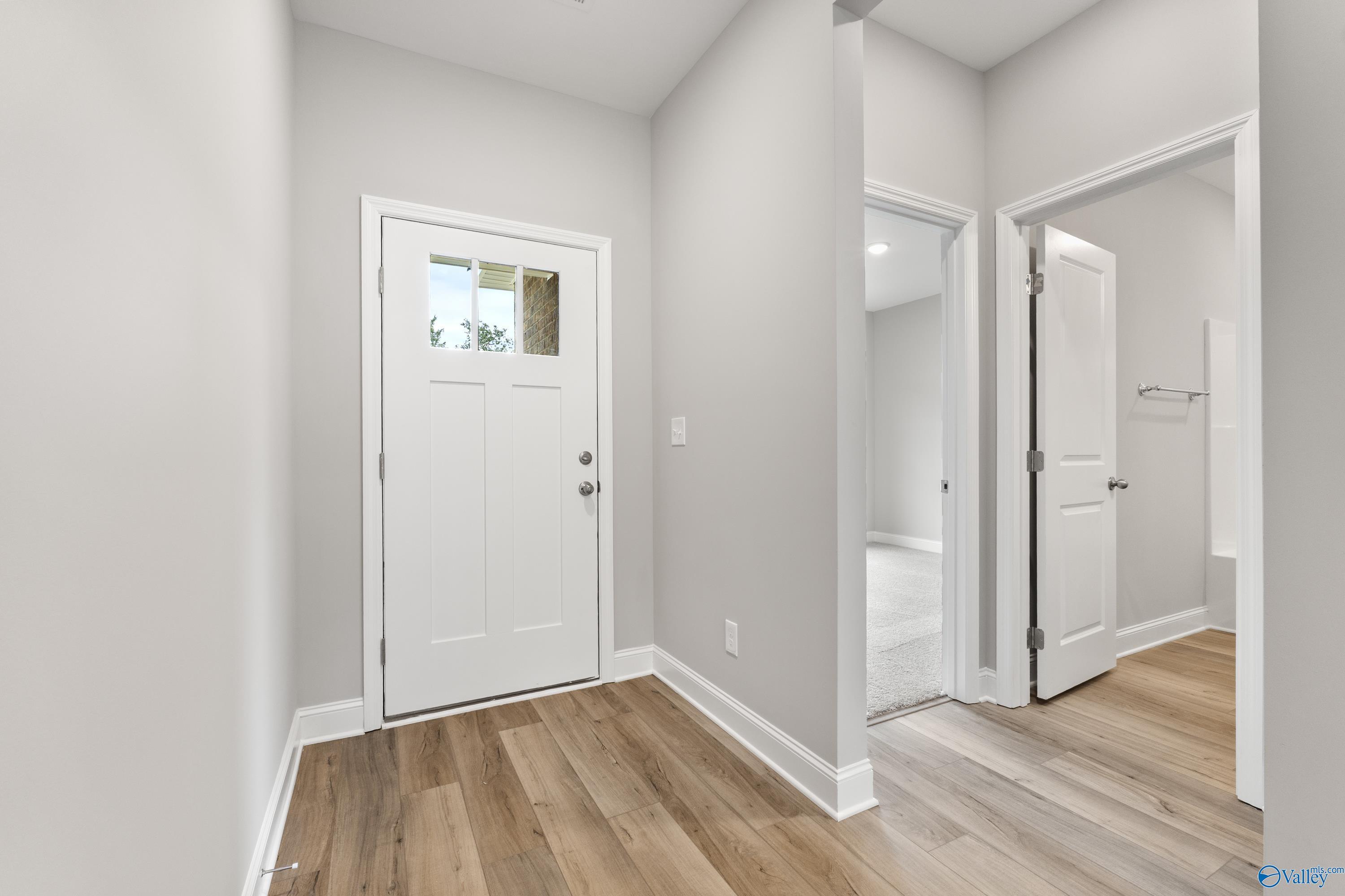 Bright entry hallway with white glass-panel door, open bathroom, and hardwood floors in 3-bedroom Davidson Homes The Franklin C, Huntsville, Alabama