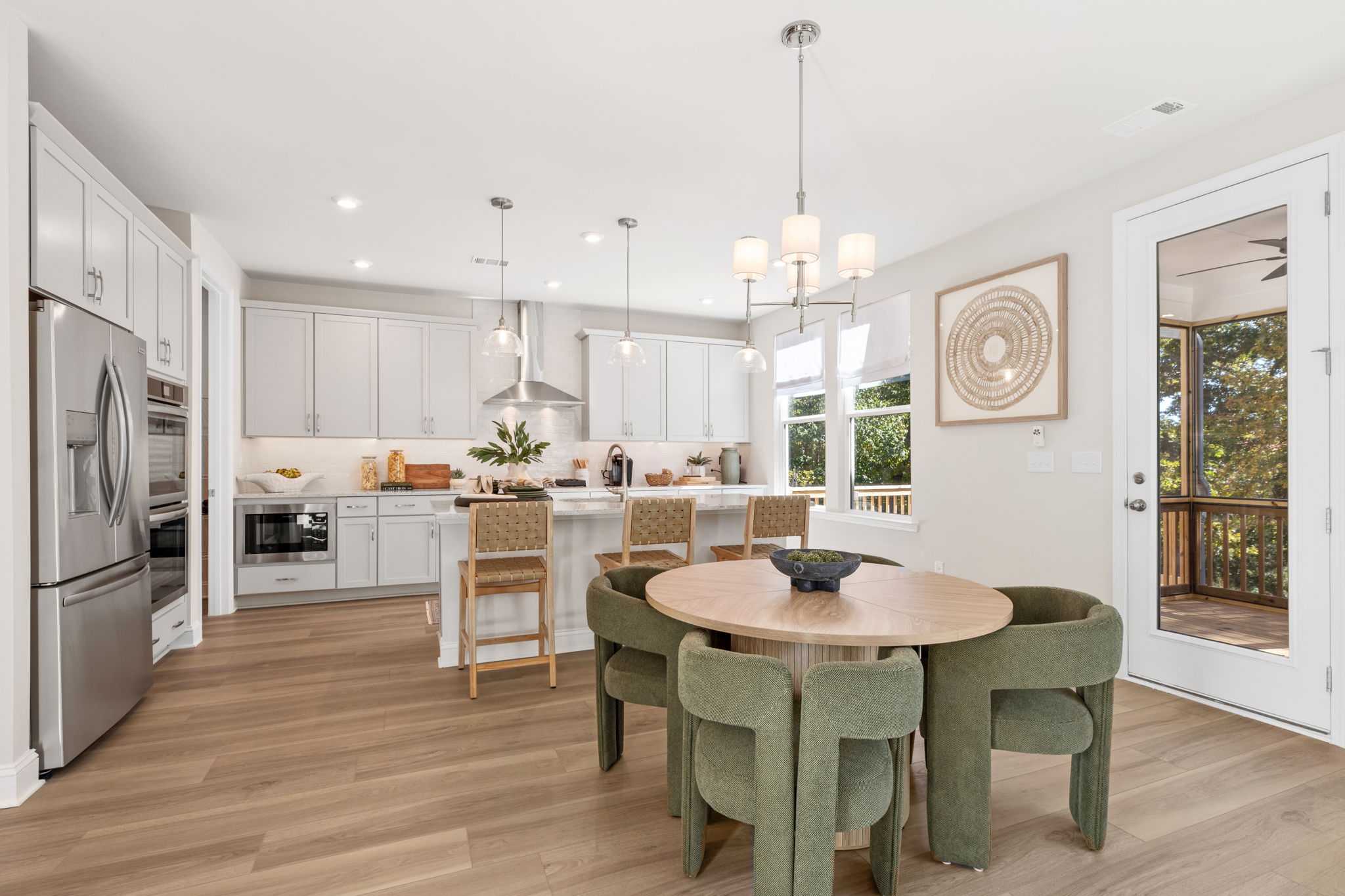 Open-concept kitchen and dining at Melody Lakeside Estates in Buford GA featuring white cabinets, island bar, round table with green chairs, hardwood floors