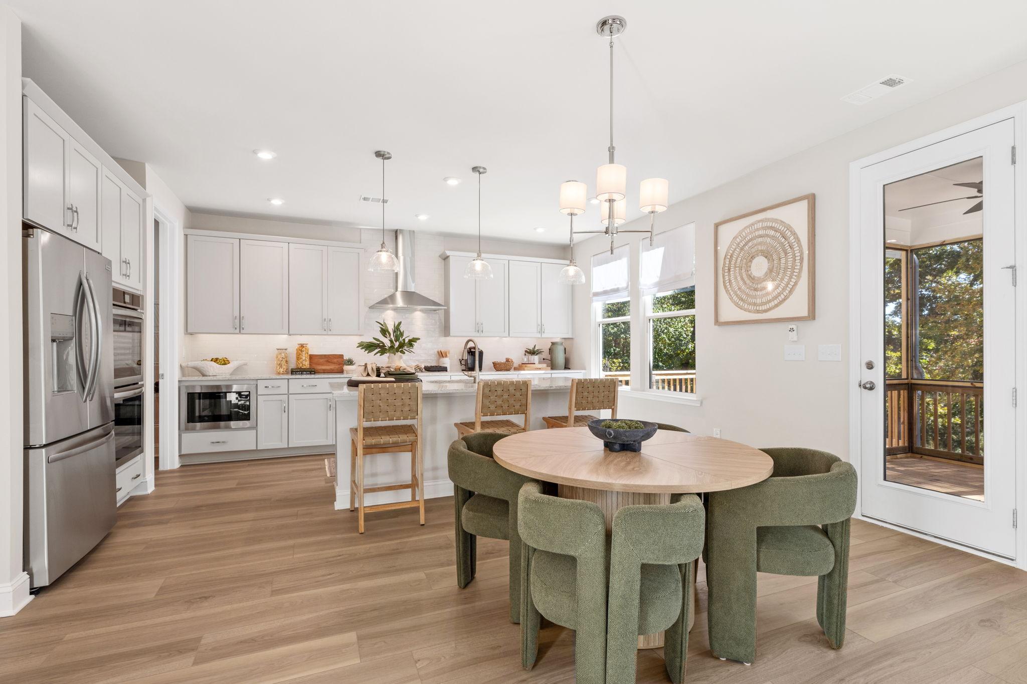 Bright kitchen with white cabinets, stainless steel appliances, quartz countertops and dining room with green chairs