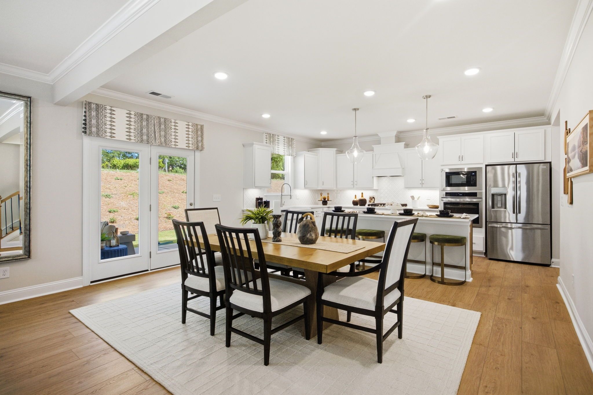 Open-concept kitchen dining area at Enclave at Belmont in Belmont NC with white cabinets, hardwood floors, and French doors to greenery