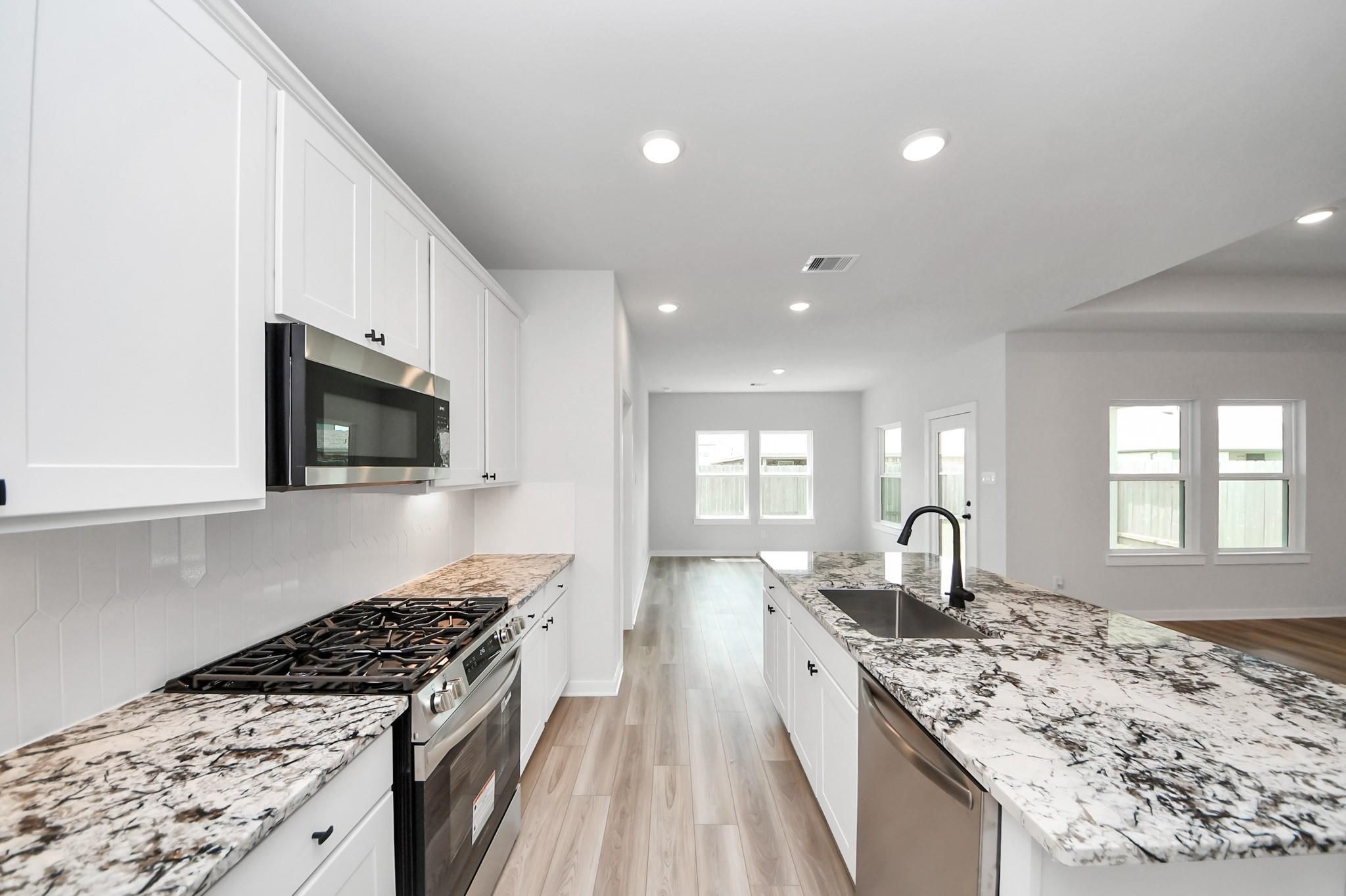 Modern kitchen with granite island and white cabinets in The Everett C floor plan at River Ranch Meadows, Dayton, Texas.
