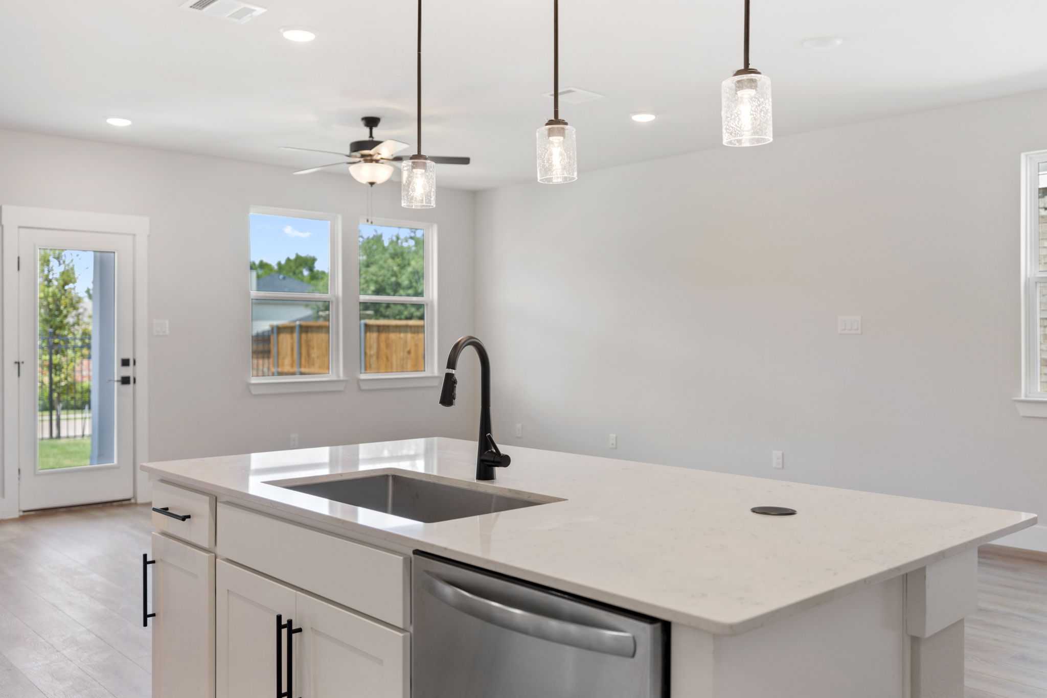 Modern kitchen with white quartz island, black faucet, stainless dishwasher, pendant lights in Davidson Homes The Durham C, Wylie TX