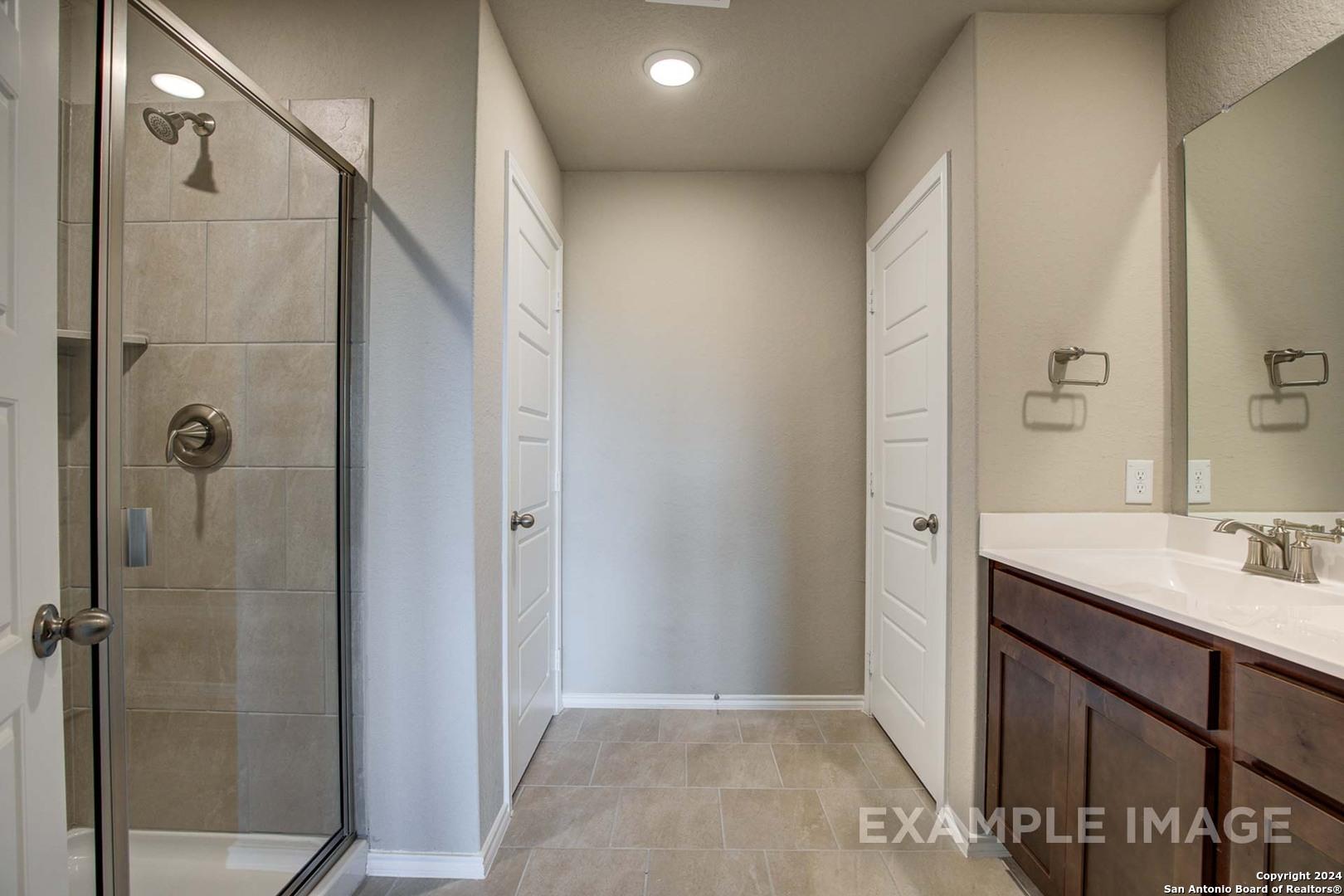 Modern master bathroom featuring glass shower enclosure, double vanity with mirrors, and neutral tile in Davidson Homes The Murray J, San Antonio