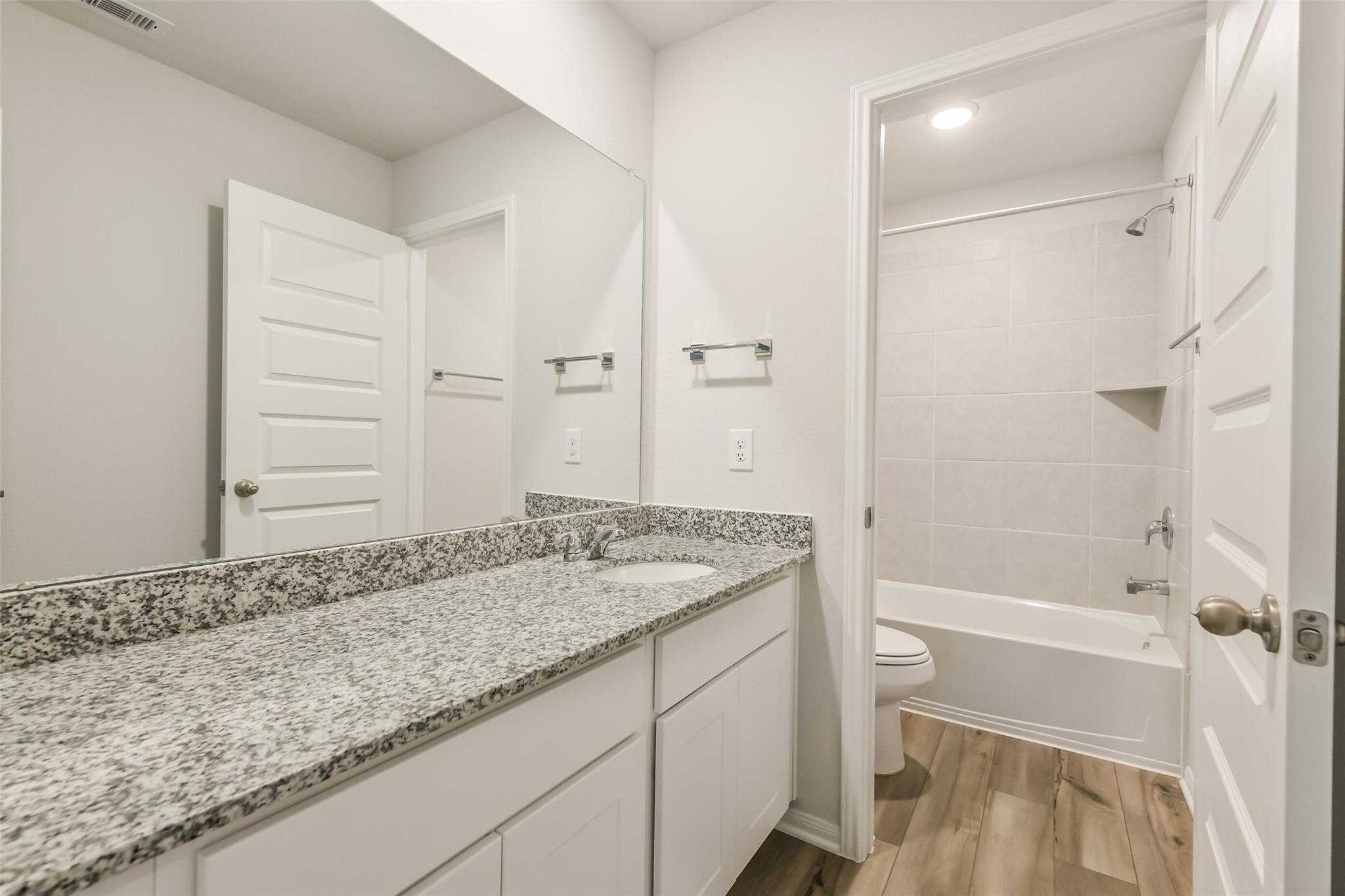 Modern bathroom with granite countertop vanity, sink, mirror, bathtub shower, and wood floors in Davidson Homes The Brazos F, Conroe TX