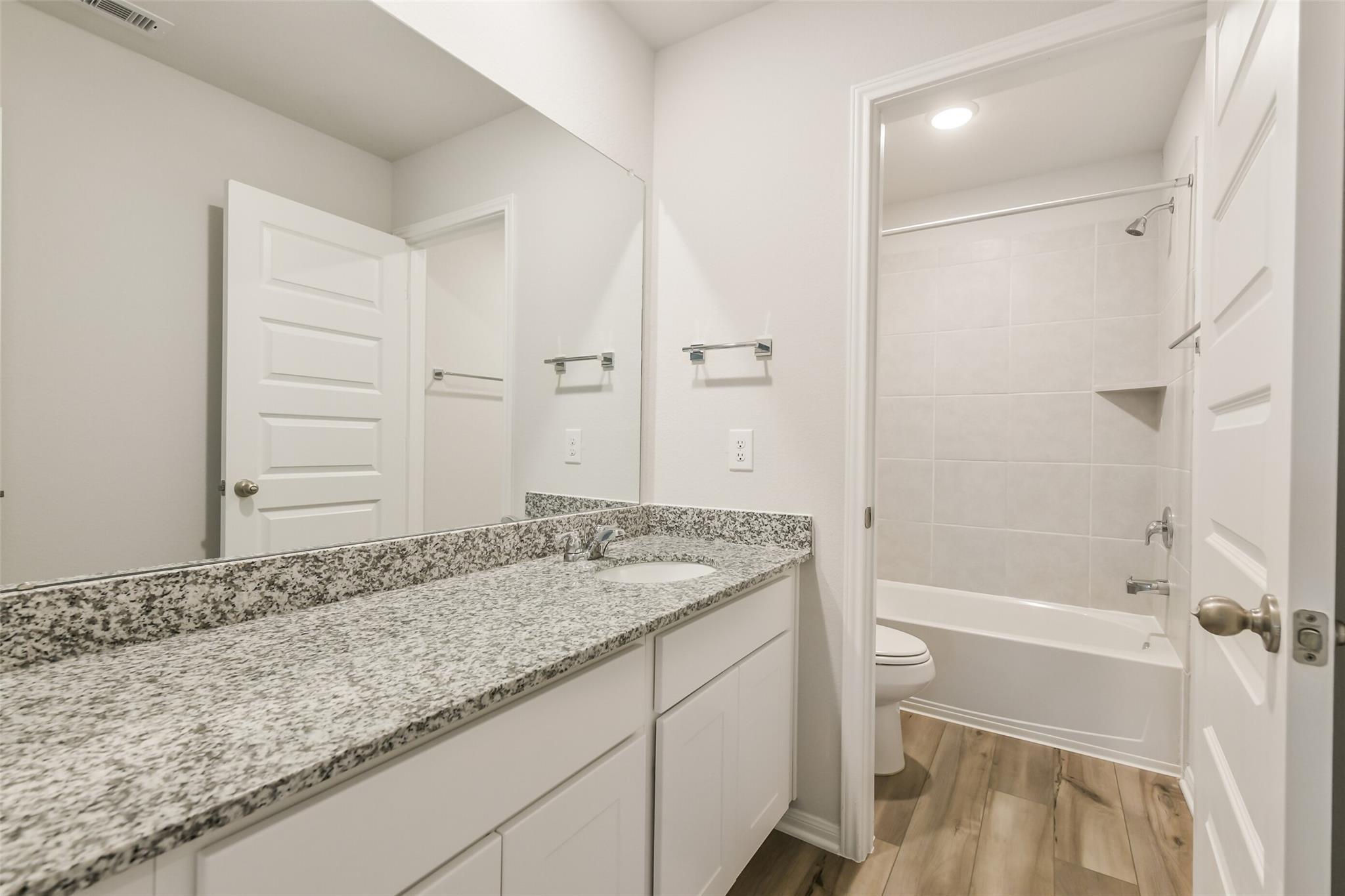Modern secondary bathroom with granite countertop vanity, subway tile tub-shower combo in Davidson Homes The Brazos F, Conroe TX