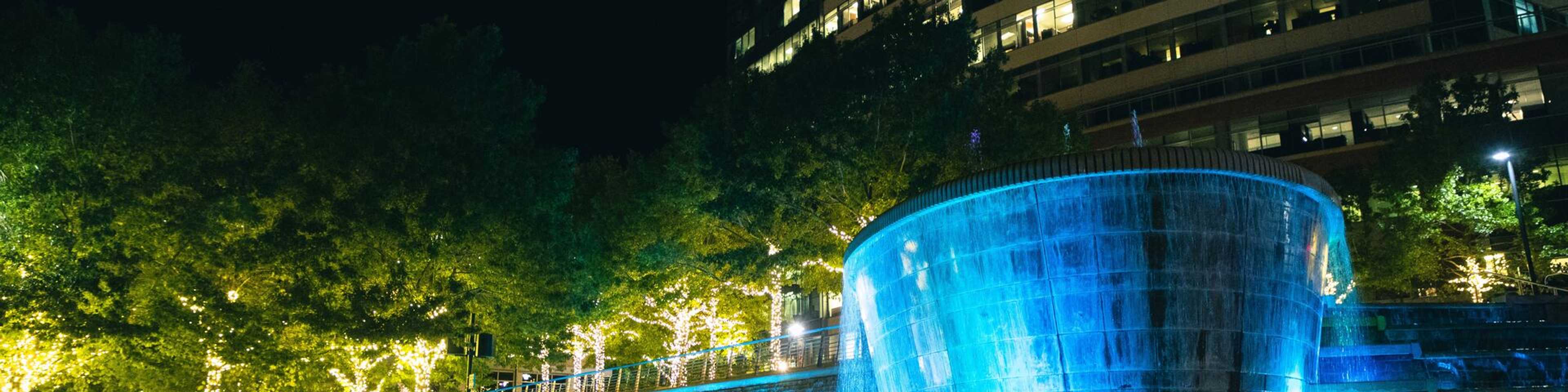 Illuminated blue fountain with cascading water and lit trees in modern The Woodlands community at night