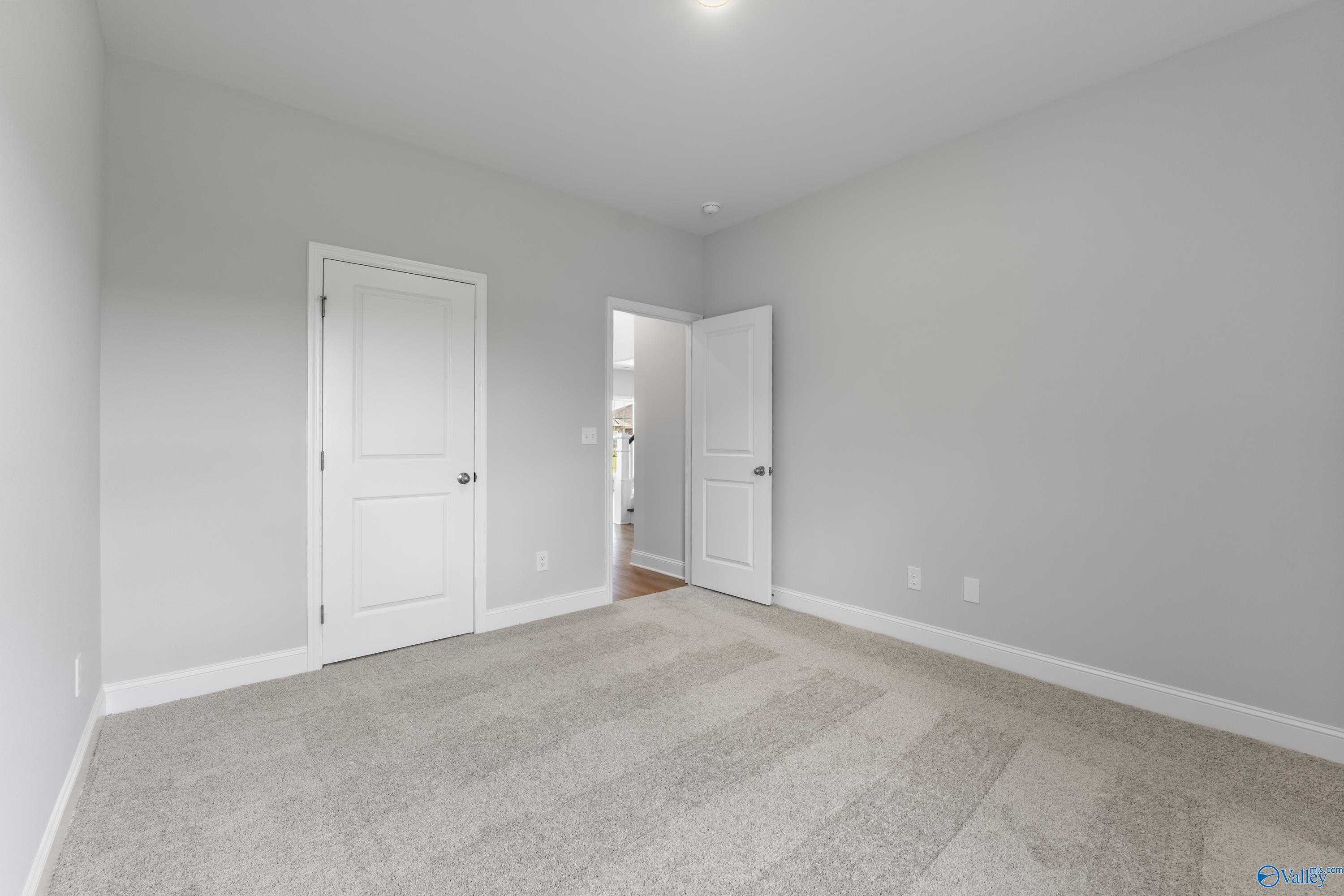 Spacious secondary bedroom with light gray walls, white doors, and carpet floor in Davidson Homes The Madison A, Toney, Alabama