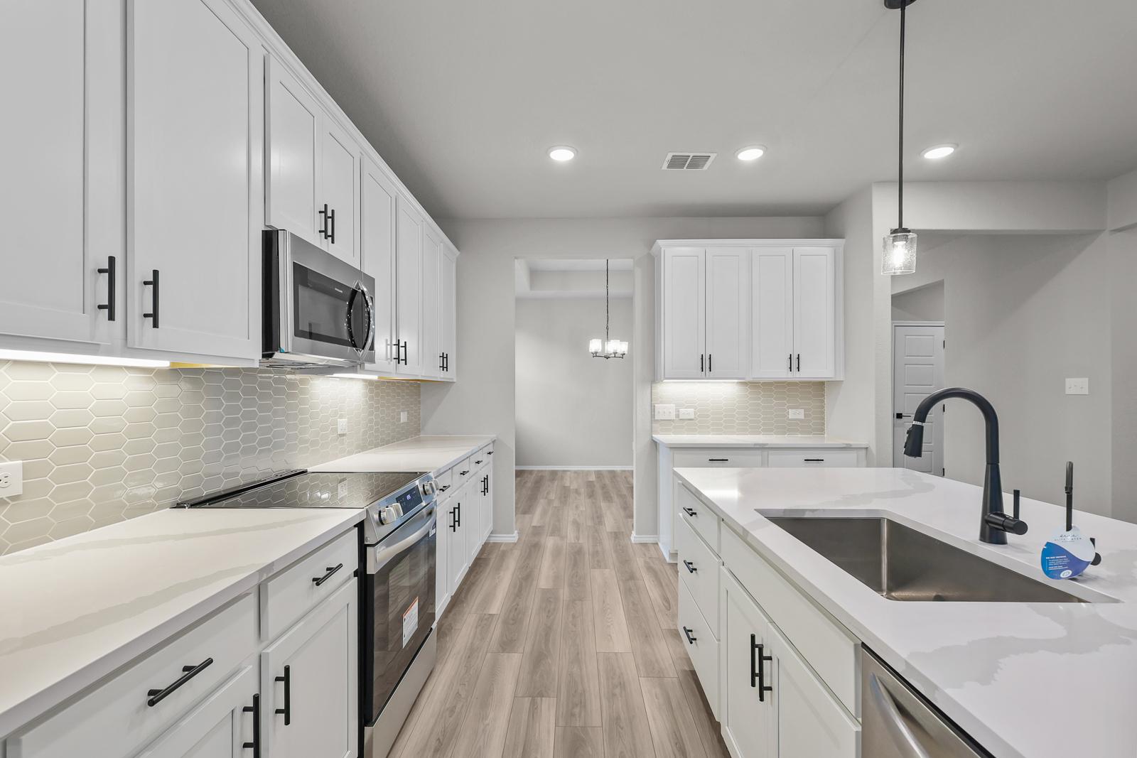 Modern kitchen in The Glenwood featuring white shaker cabinets, quartz countertops, and a central island in Seguin, Texas.
