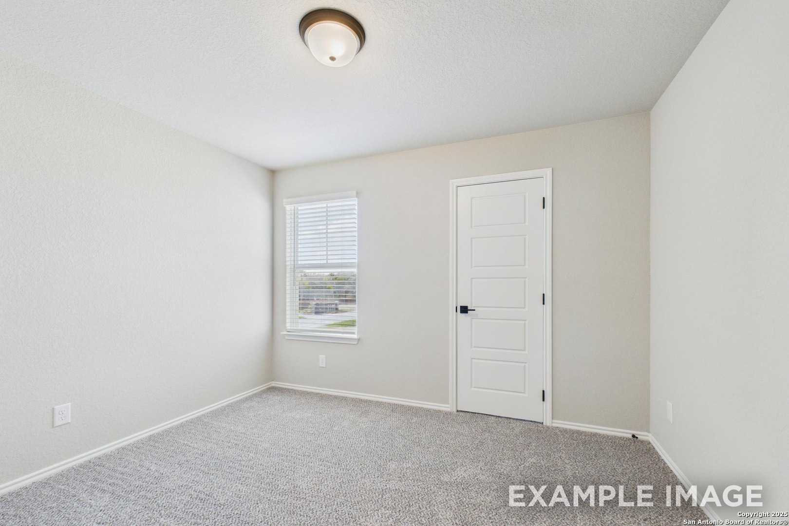 Empty bedroom with beige walls, gray carpet, window blinds, and white door in Davidson Homes The Charlotte A, San Antonio, Texas