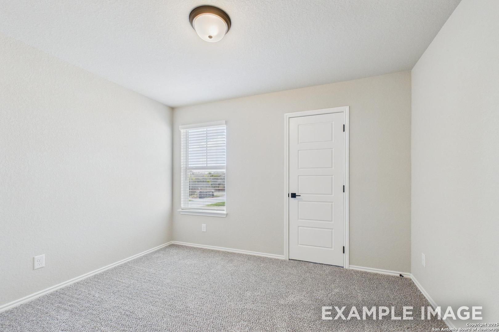Empty bedroom with beige walls, gray carpet, window blinds, and white door in Davidson Homes The Charlotte B, San Antonio, Texas