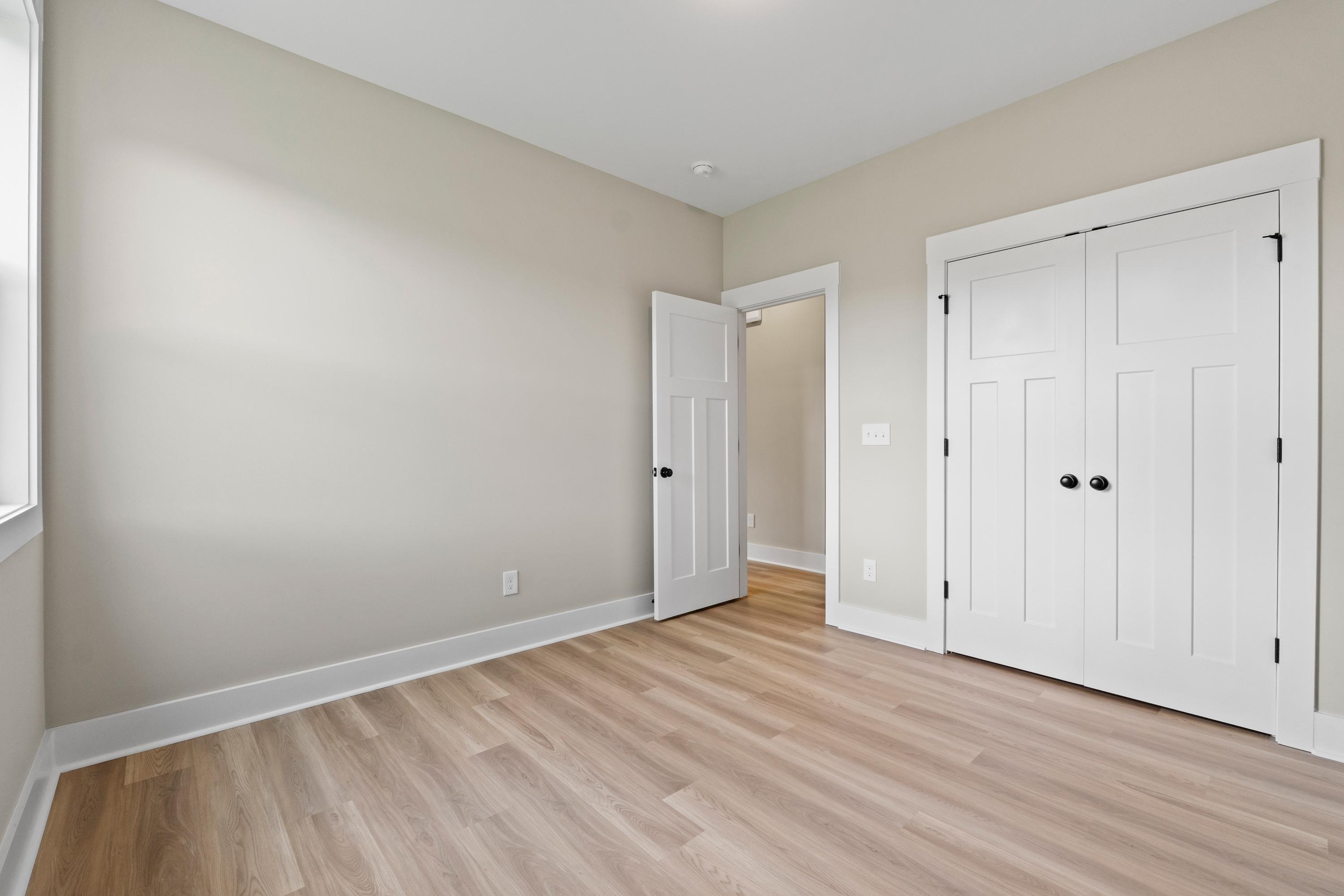 Spacious bedroom in The Oxford B with beige walls, oak hardwood floors, white double closet doors, and adjacent bath access