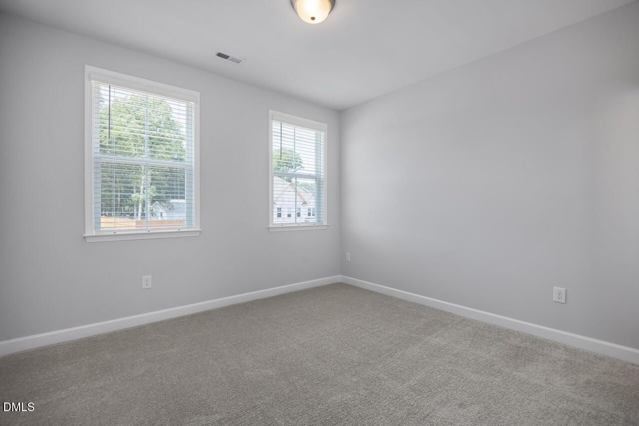Bright, carpeted bedroom with neutral walls and double windows in The Ashport L at Sage on North Main, Wake Forest, NC.