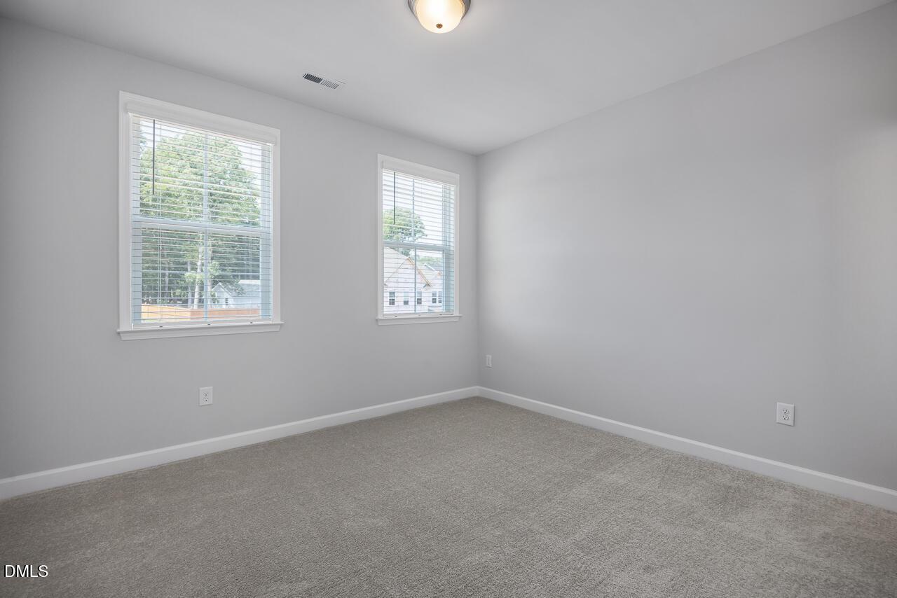 Bright, carpeted bedroom with neutral walls and double windows in The Ashport L at Sage on North Main, Wake Forest, NC.