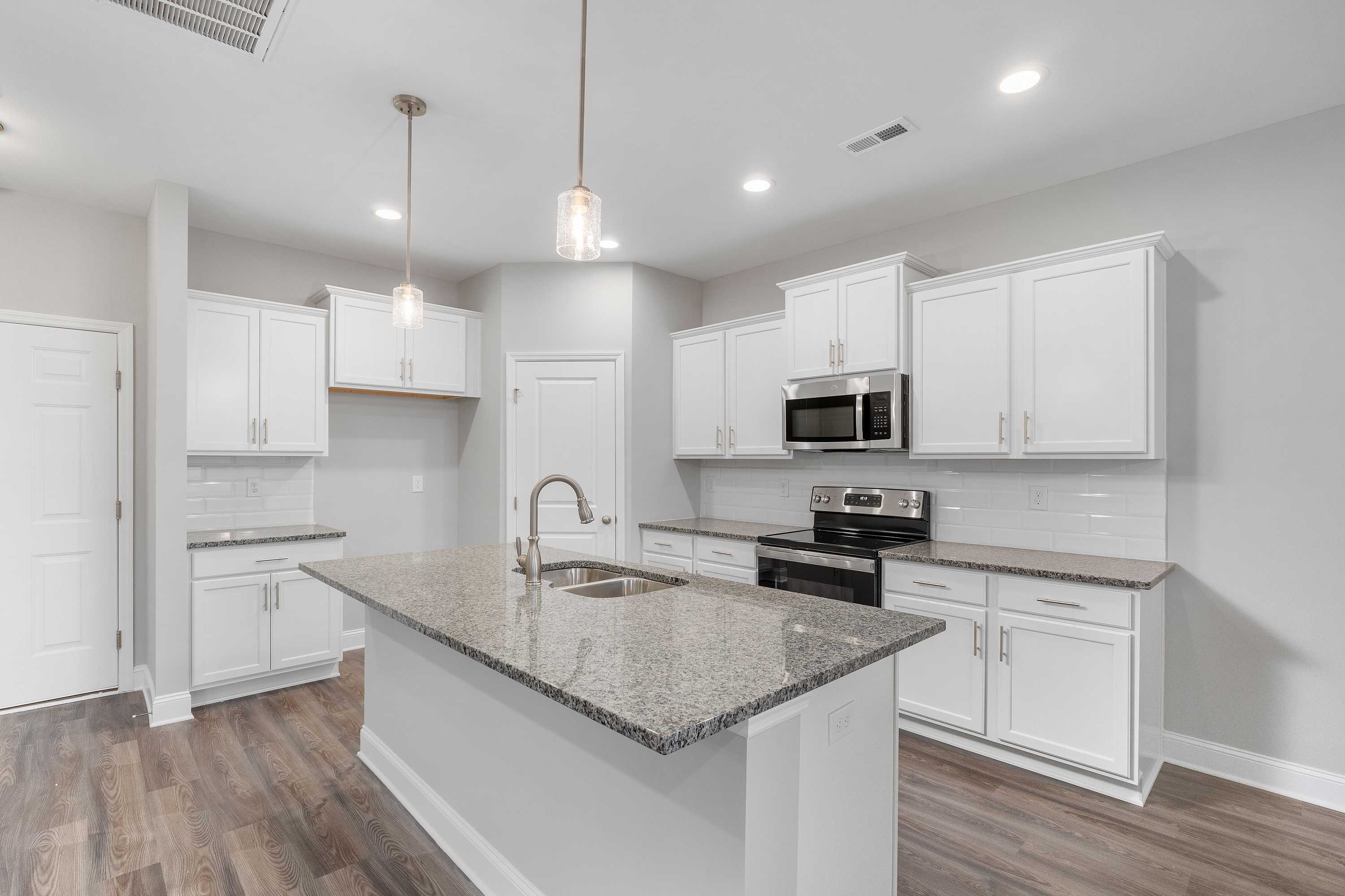 Spacious kitchen in The Aiken by Davidson Homes with white cabinets, granite island sink, stainless appliances, hardwood floors