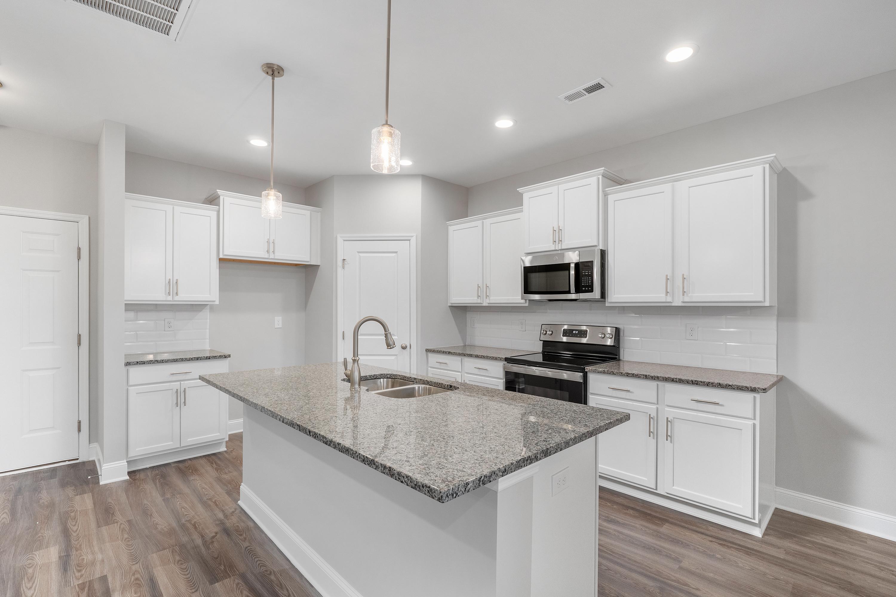 Spacious kitchen in The Aiken by Davidson Homes with white cabinets, granite island sink, stainless appliances, hardwood floors