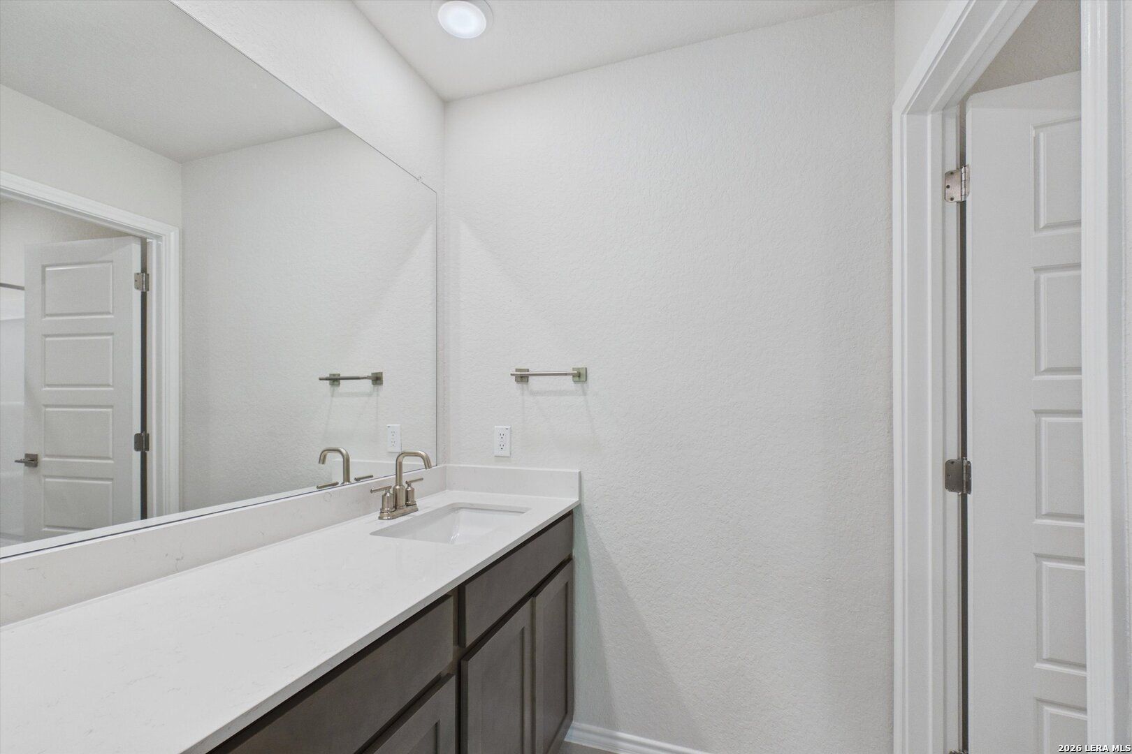 Modern bathroom vanity with white countertop and dark cabinetry in The Charlotte B floor plan, Meadows at Oak Creek.