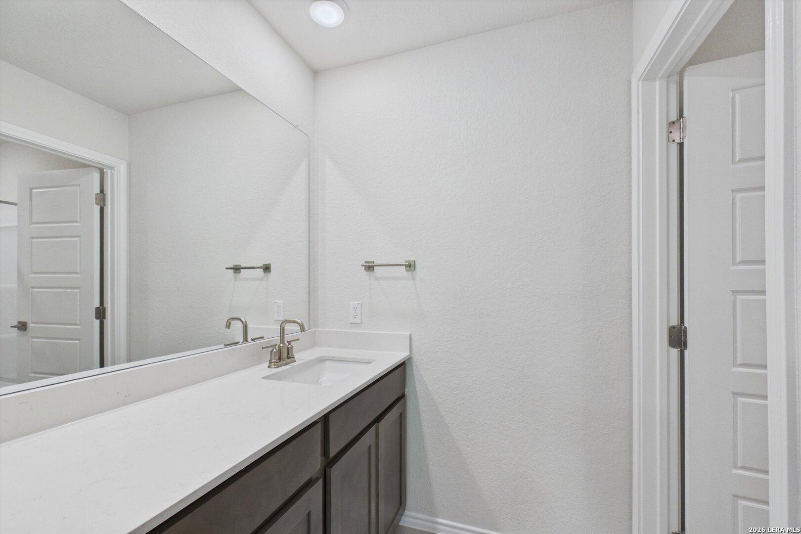 Modern bathroom vanity with white countertop and dark cabinetry in The Charlotte B floor plan, Meadows at Oak Creek.