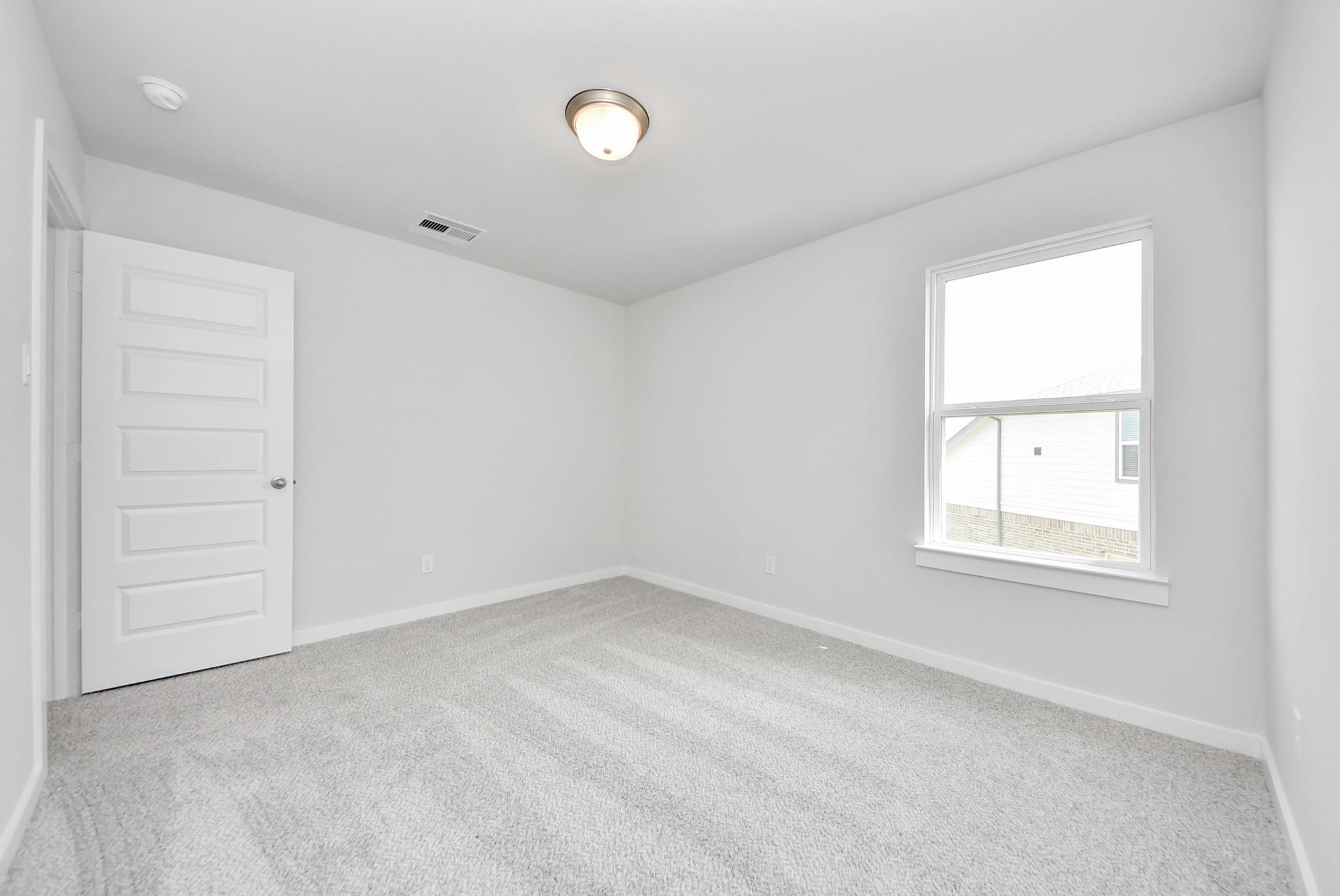 Bright, neutral-toned secondary bedroom with plush carpeting in The Verano B floor plan at Sunterra, Katy, Texas.