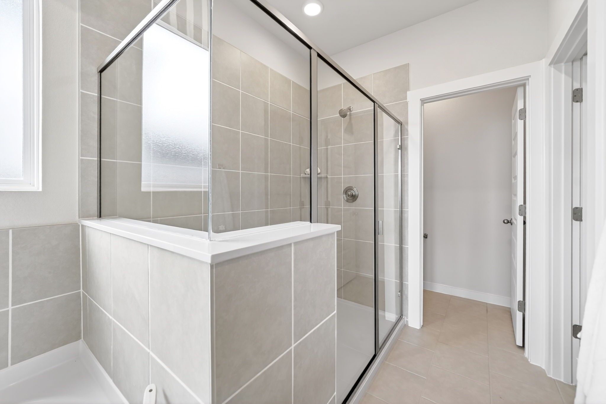 Modern walk-in glass shower with neutral tile in a Davidson Homes The Laurel M floor plan at Parks at Foster Crossing.