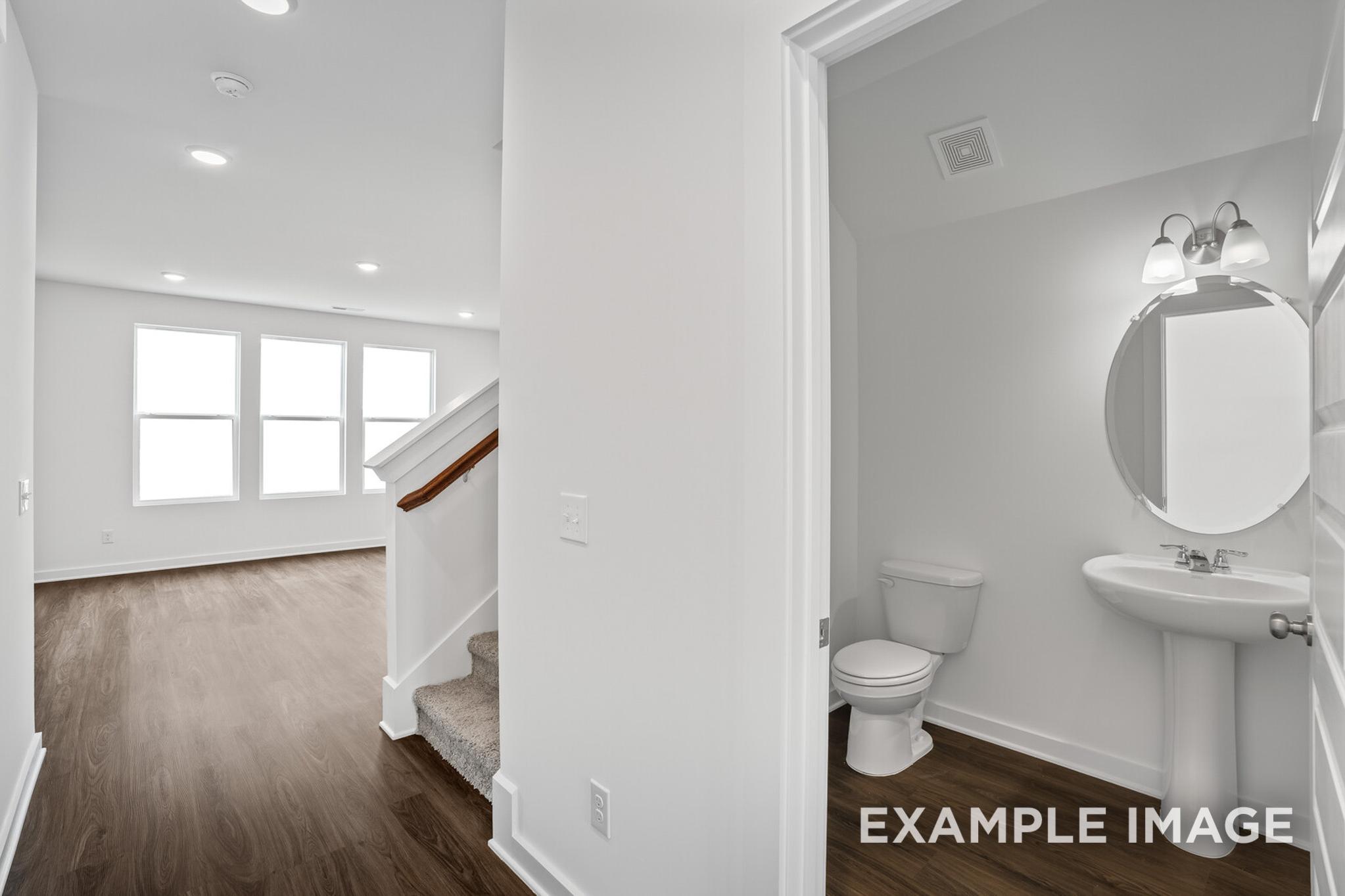 Spacious hallway in The Logan home design with open staircase, large windows, and adjacent white powder room featuring sink and toilet