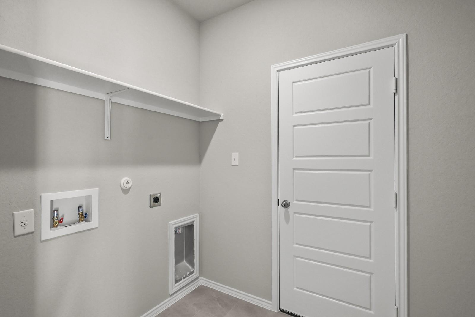 Laundry room with utility connections and built-in shelving in The Frio G floor plan by Davidson Homes in Heartland, TX.