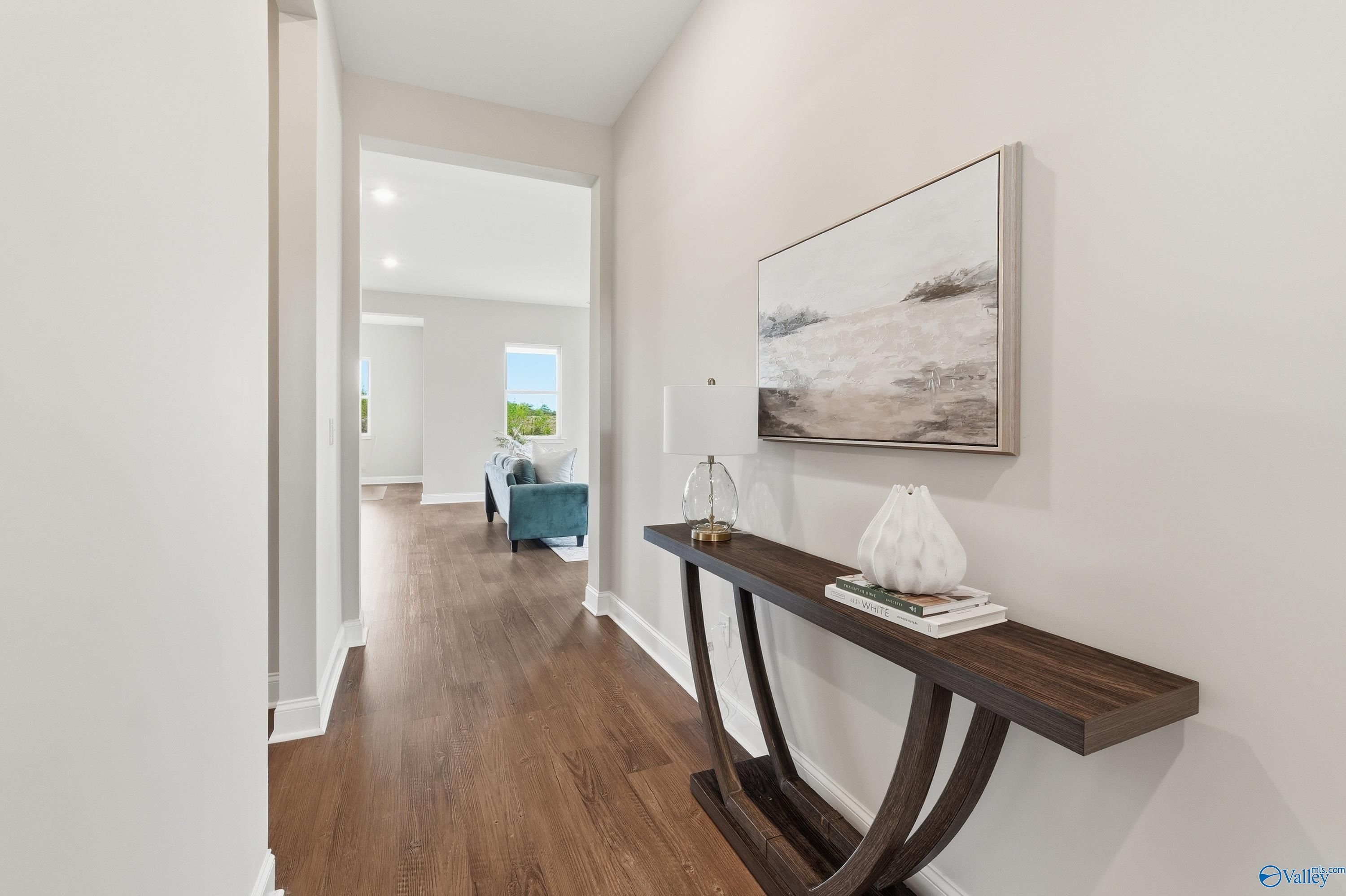 Elegant hallway with light wood floors, dark console table, abstract painting, and blue sofa in Davidson Homes Arcadia B, Huntsville AL