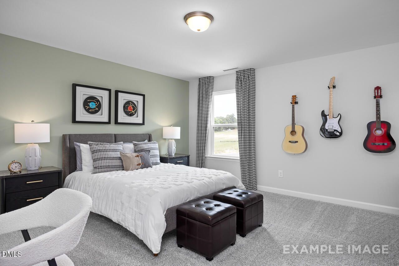 Cozy bedroom with hanging guitars, white bedding, green walls in Davidson Homes The Magnolia D, Angier, NC