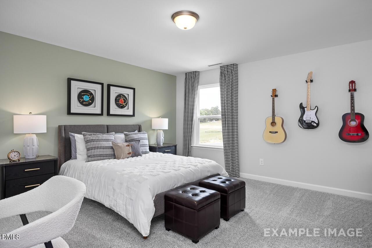 Cozy bedroom with hanging guitars, white bedding, green walls in Davidson Homes The Magnolia D, Angier, NC