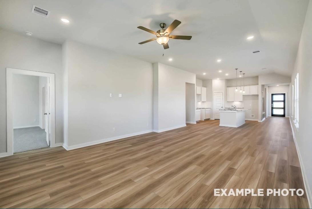 Open-concept living and kitchen with light wood floors, white cabinets, island sink, and ceiling fan in Davidson Homes Riviera C, Dayton Texas