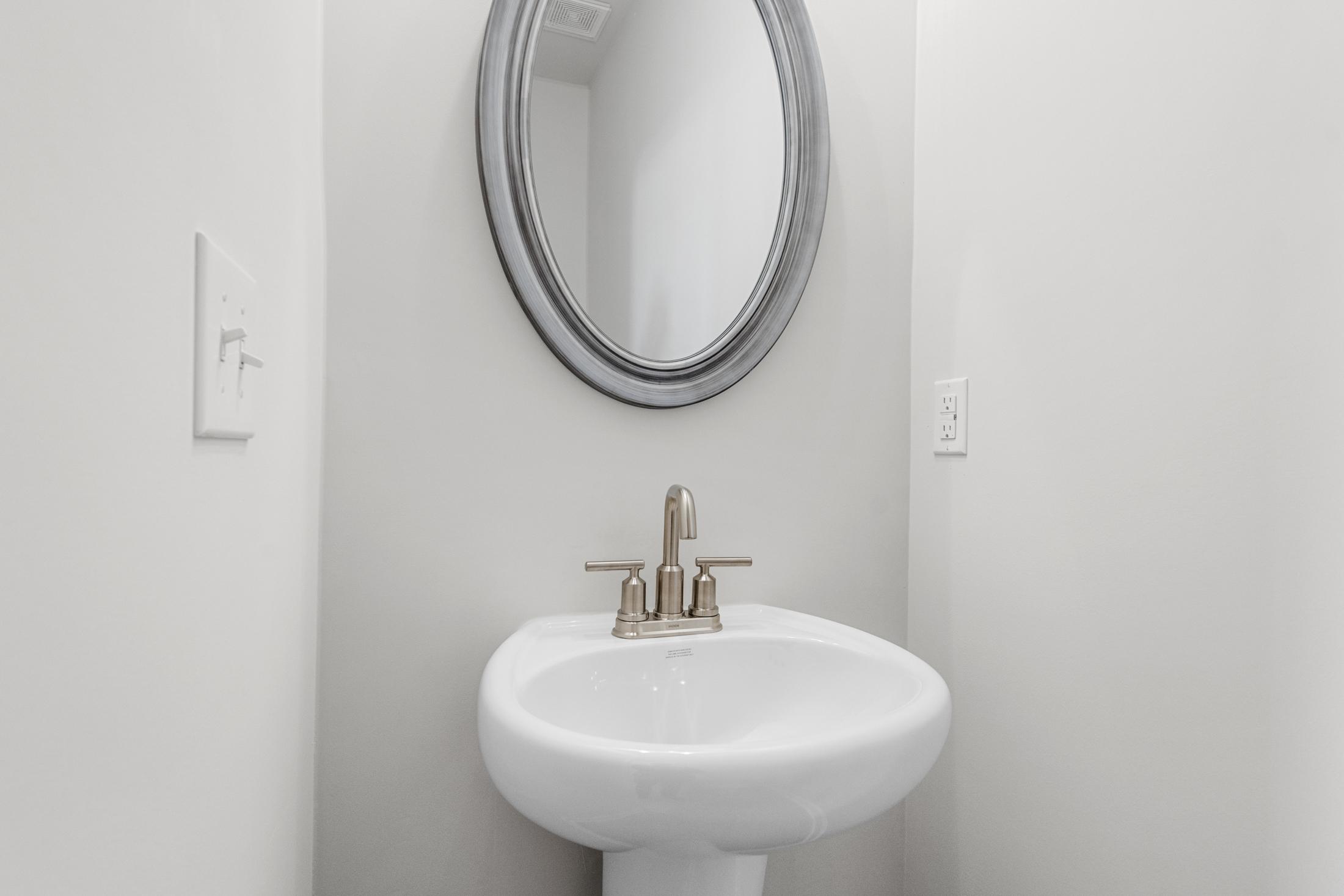White pedestal sink with chrome faucet and round silver-framed mirror in The Glenwood A powder room