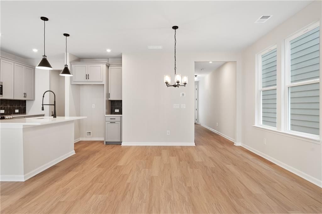 Bright open-concept kitchen with white cabinets, large island sink, pendant lights, and hardwood floors in Davidson Homes The Marion A, Kennesaw, GA
