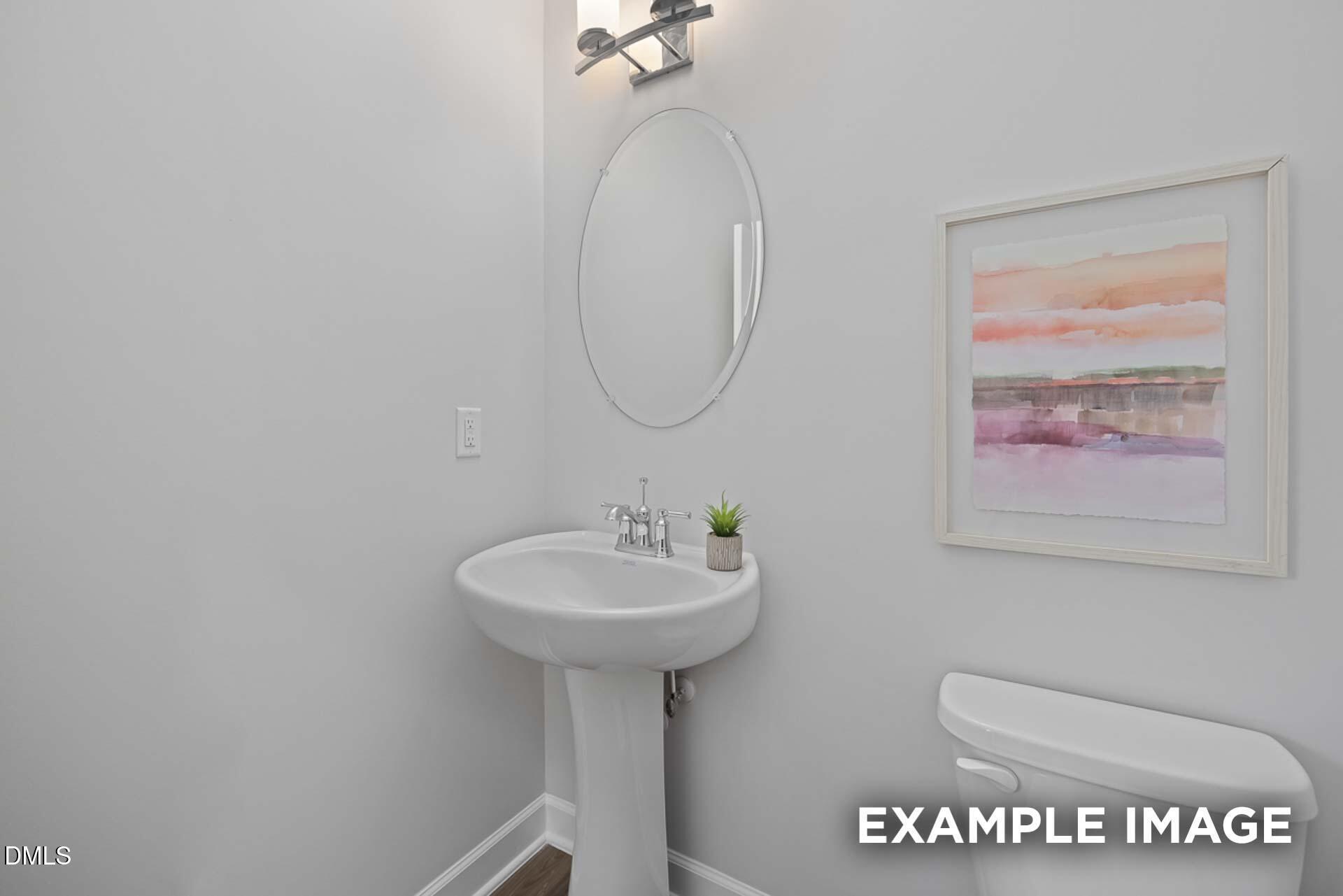 Elegant powder room featuring white pedestal sink, round mirror, and abstract wall art in Davidson Homes The Gavin C, Lillington, NC