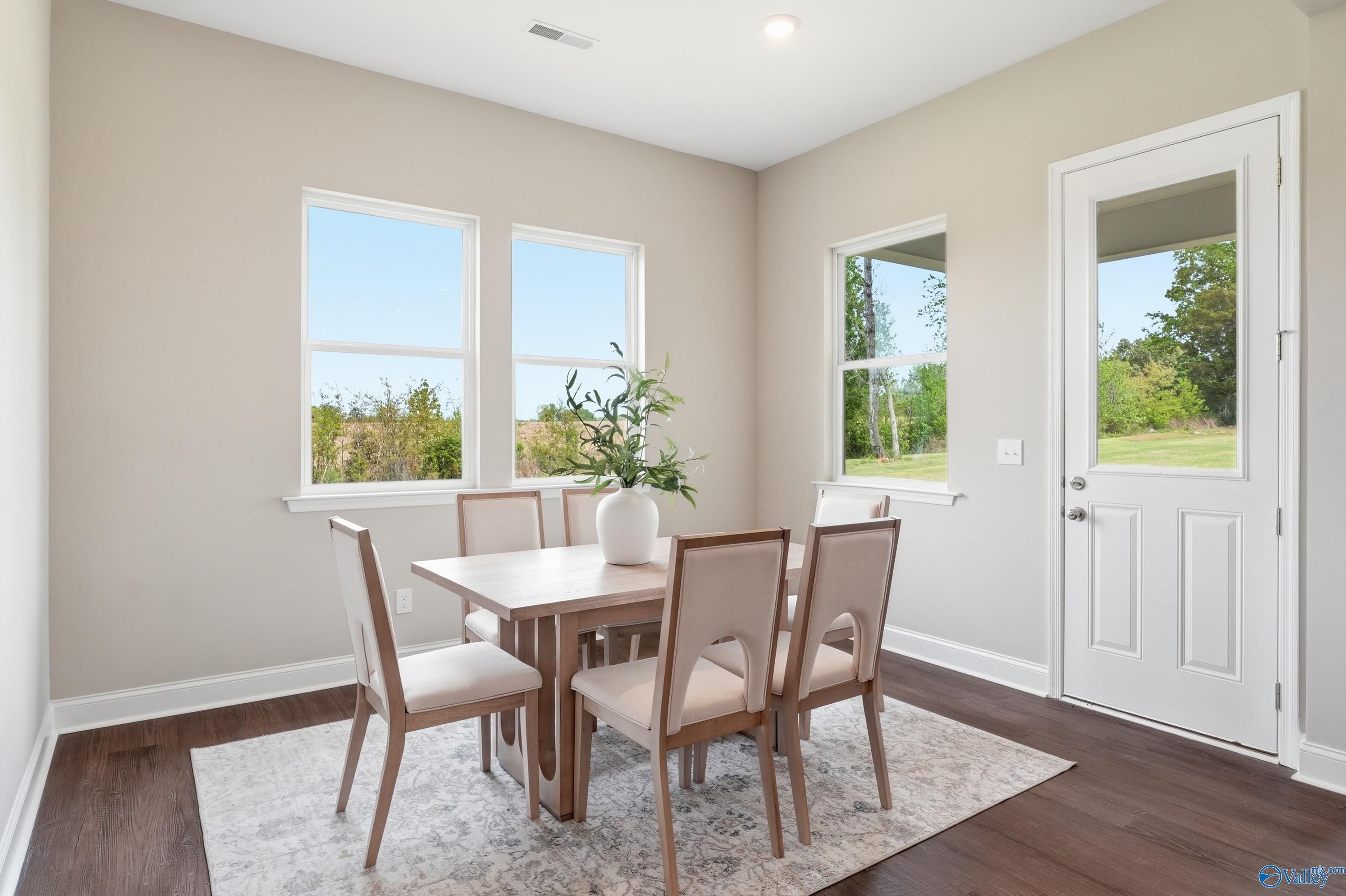 Bright dining room with wooden table, upholstered chairs, potted plant, and backyard views in The Arcadia B by Davidson Homes, Huntsville, AL