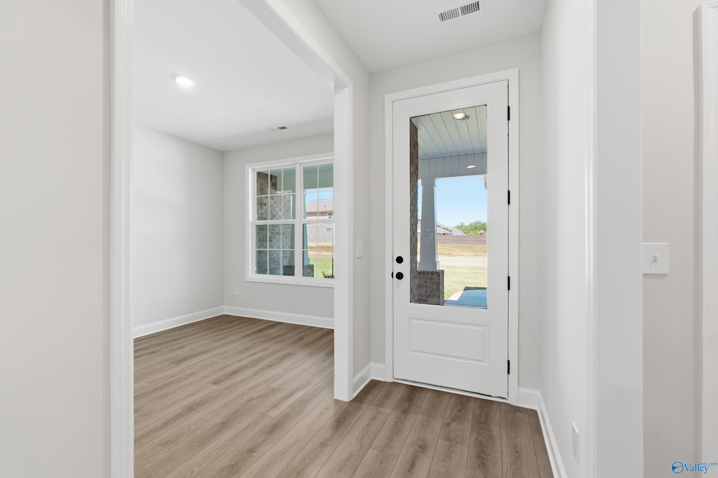 Bright living room with white walls, light hardwood floors, and glass door to covered porch in The Rockford B home, Athens AL