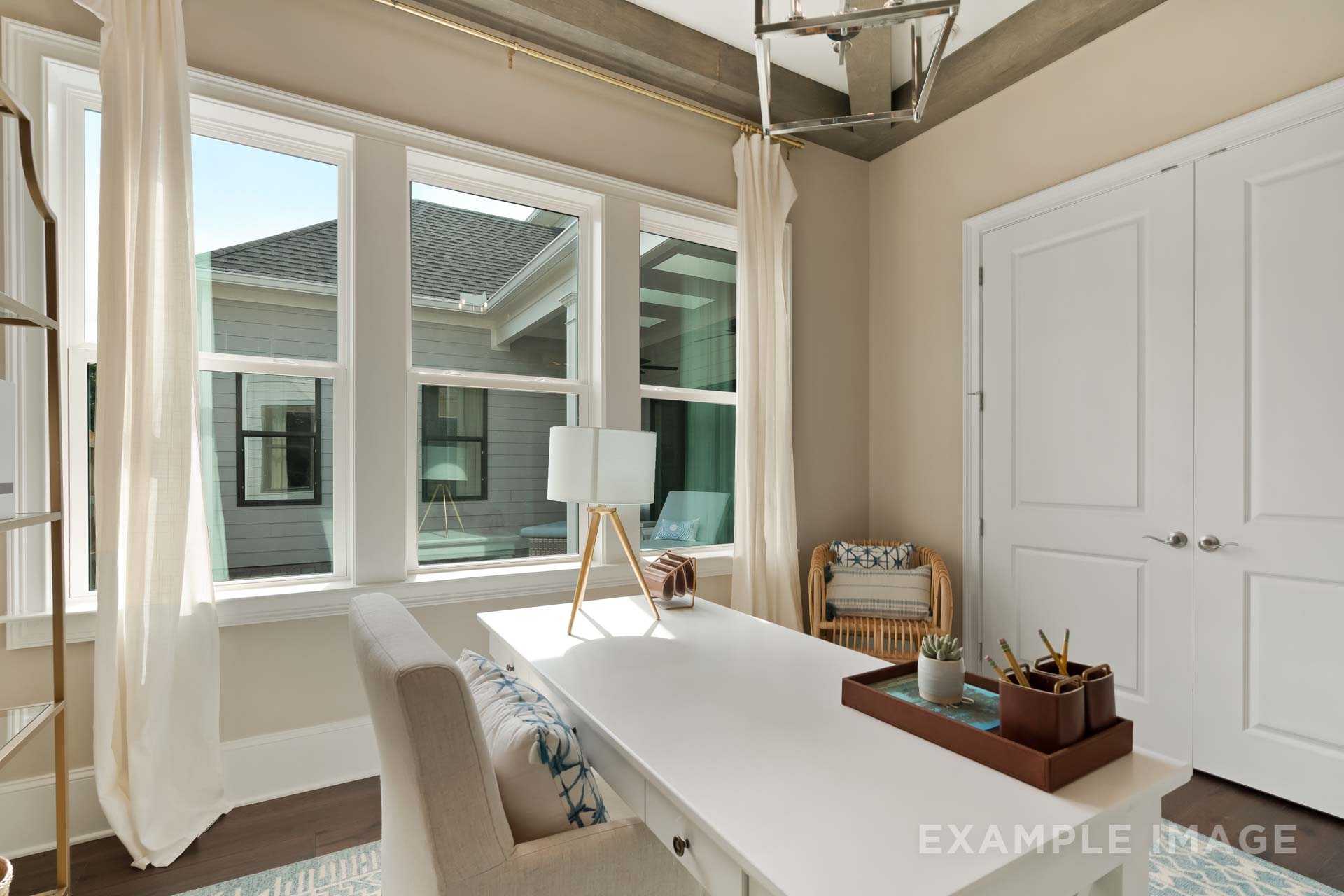 Spacious home office in The Seaside B with white desk, sheer-curtained windows, wicker chair, and neutral tones