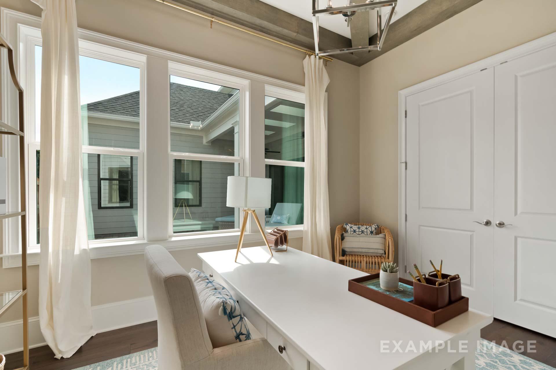Spacious home office in The Seaside C with white desk, large sunny windows, wicker chair, and built-in storage, Davidson Homes design