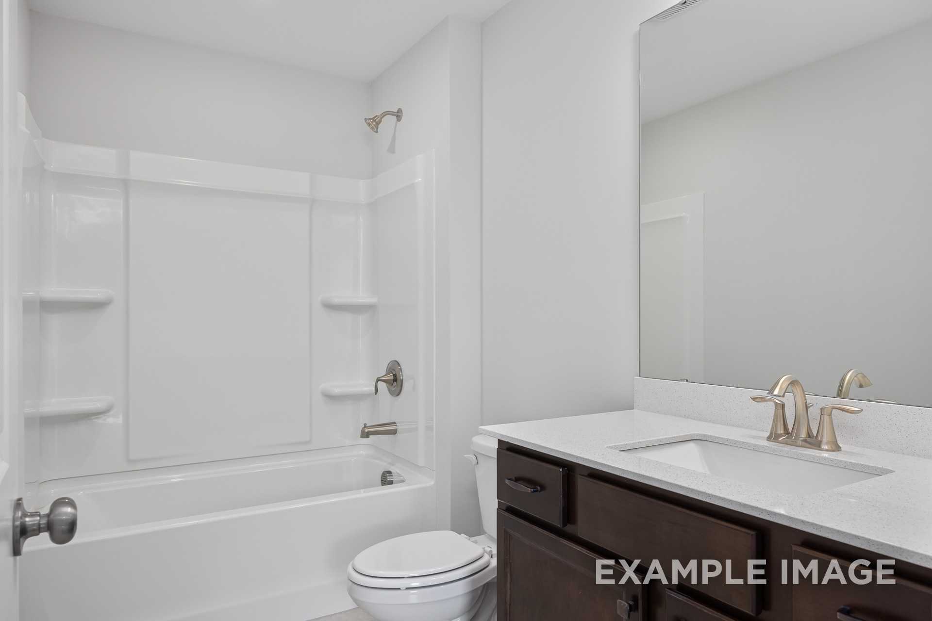 Spacious Grace C master bathroom with white tub-shower combo, brown vanity, quartz countertop, and gold fixtures