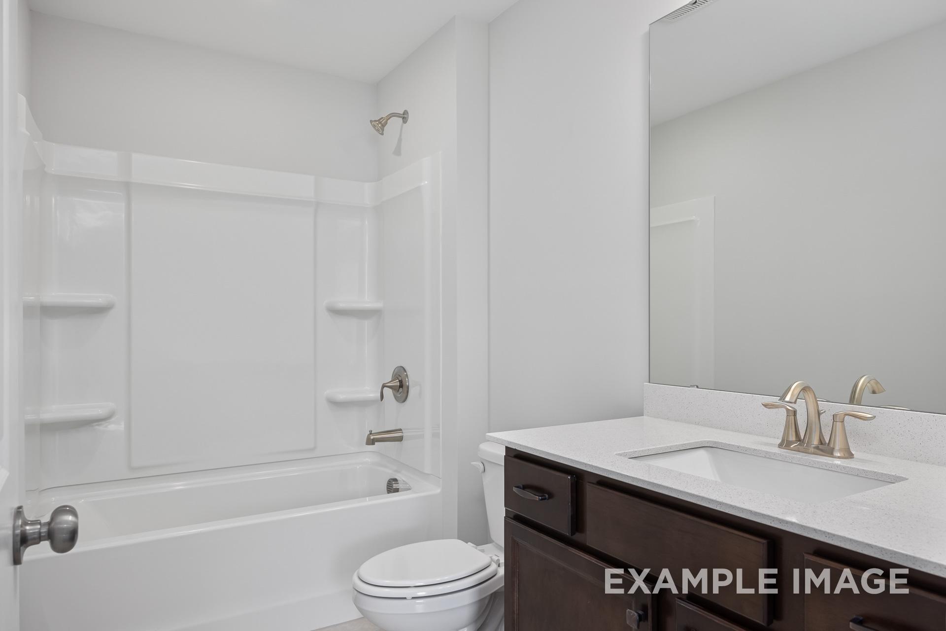 Spacious Grace C master bathroom with white tub-shower combo, brown vanity, quartz countertop, and gold fixtures